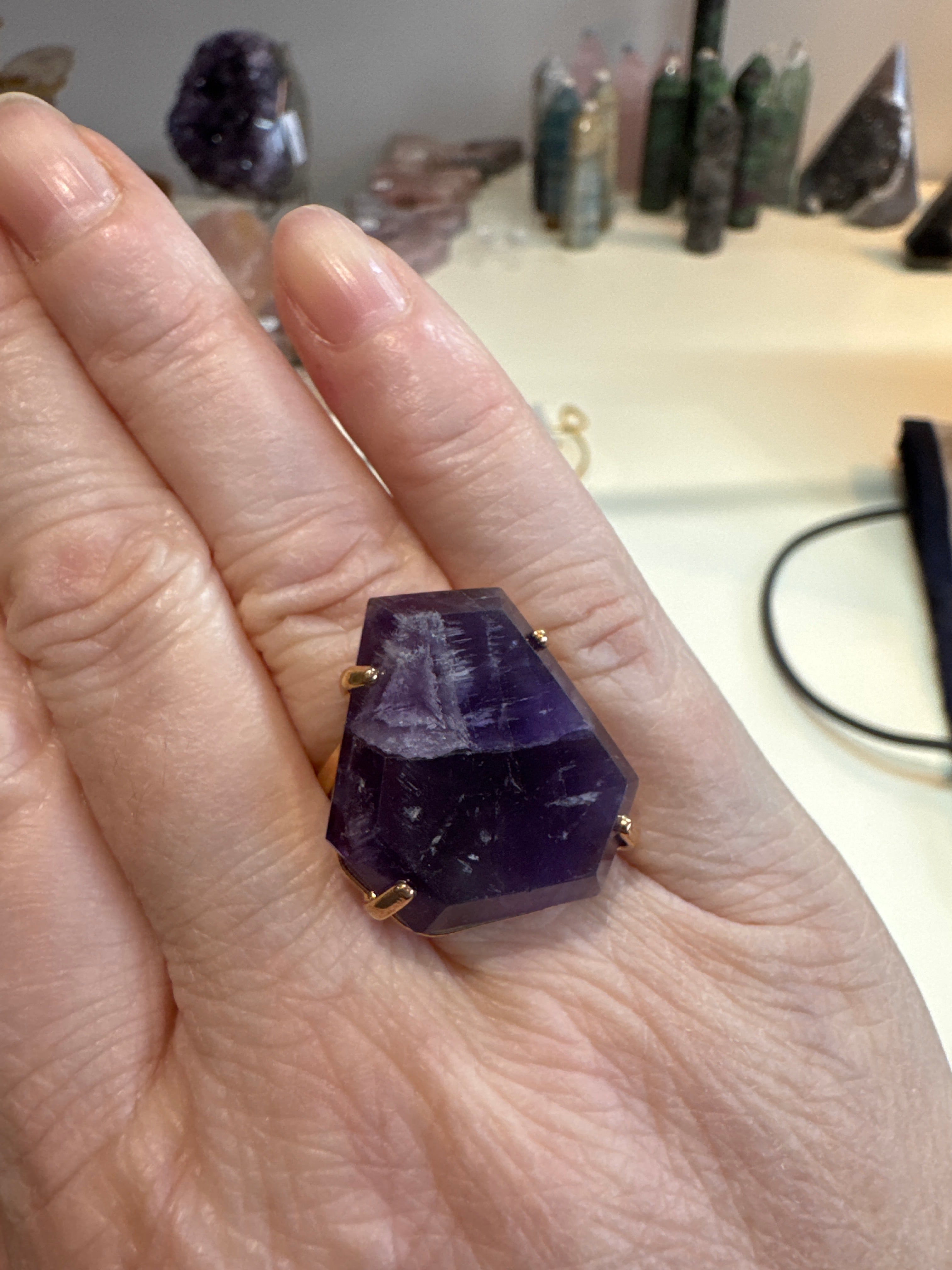 Hand wearing a purple gemstone ring with a blurred background of crystals.