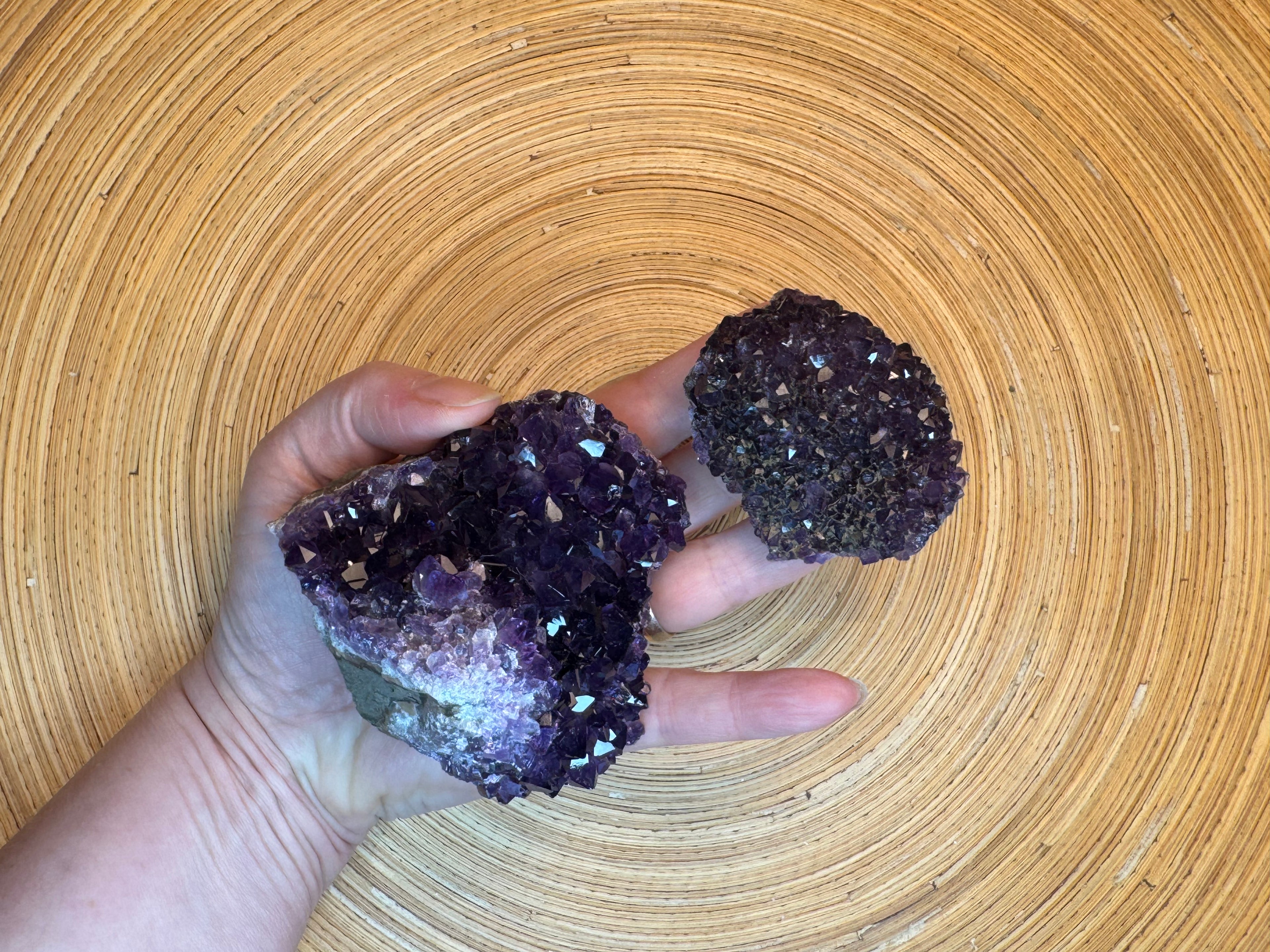 Hand holding two purple crystal rocks on a woven surface