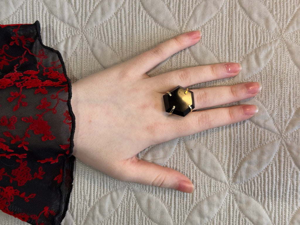Hand wearing a black obsidian and gold ring on a textured surface