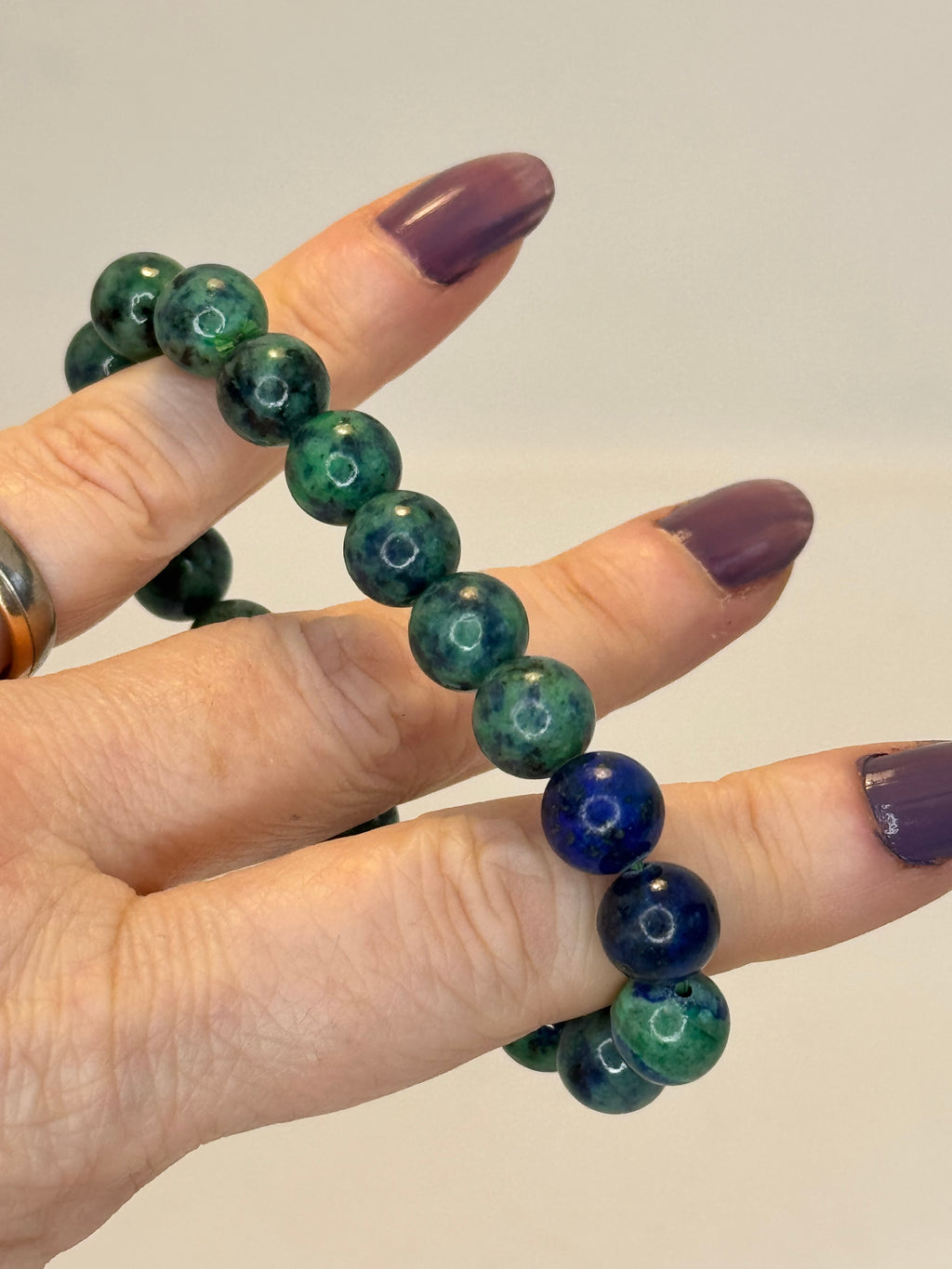 Hand wearing a bracelet with green and blue beads on a plain background