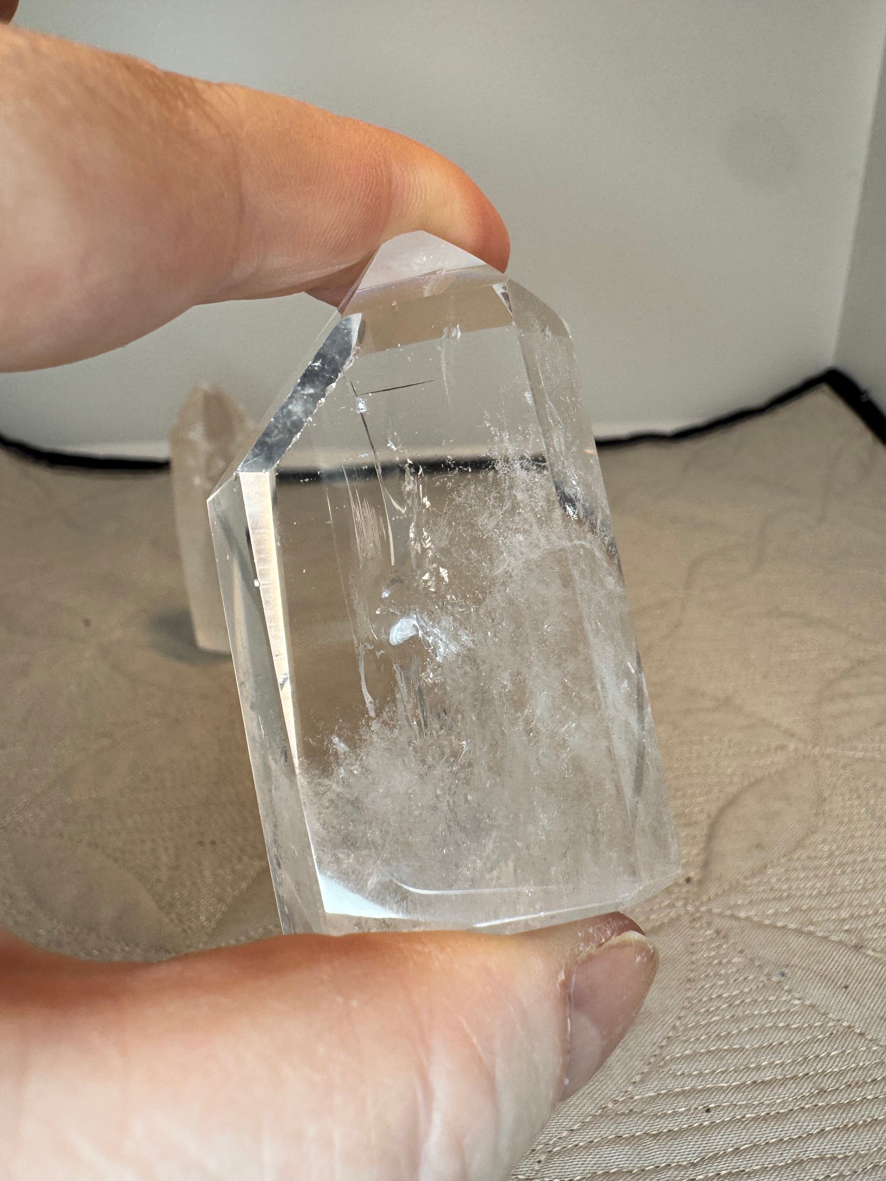 Clear crystal mini tower held between two fingers against a neutral background