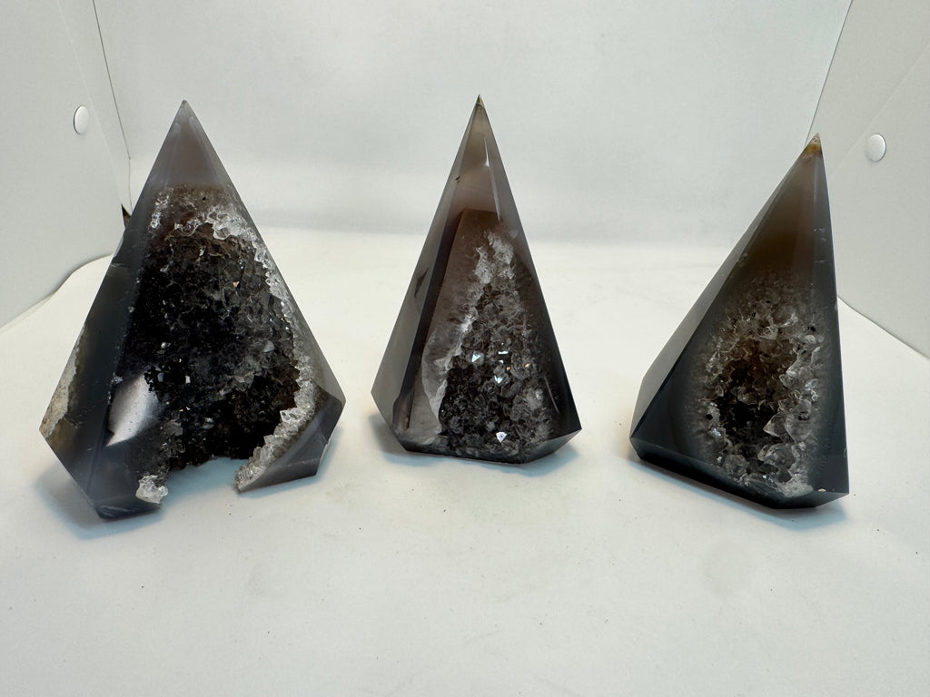 Three pyramid-shaped geode crystals on a white surface with a white background