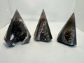 Three pyramid-shaped geode crystals on a white surface with a white background