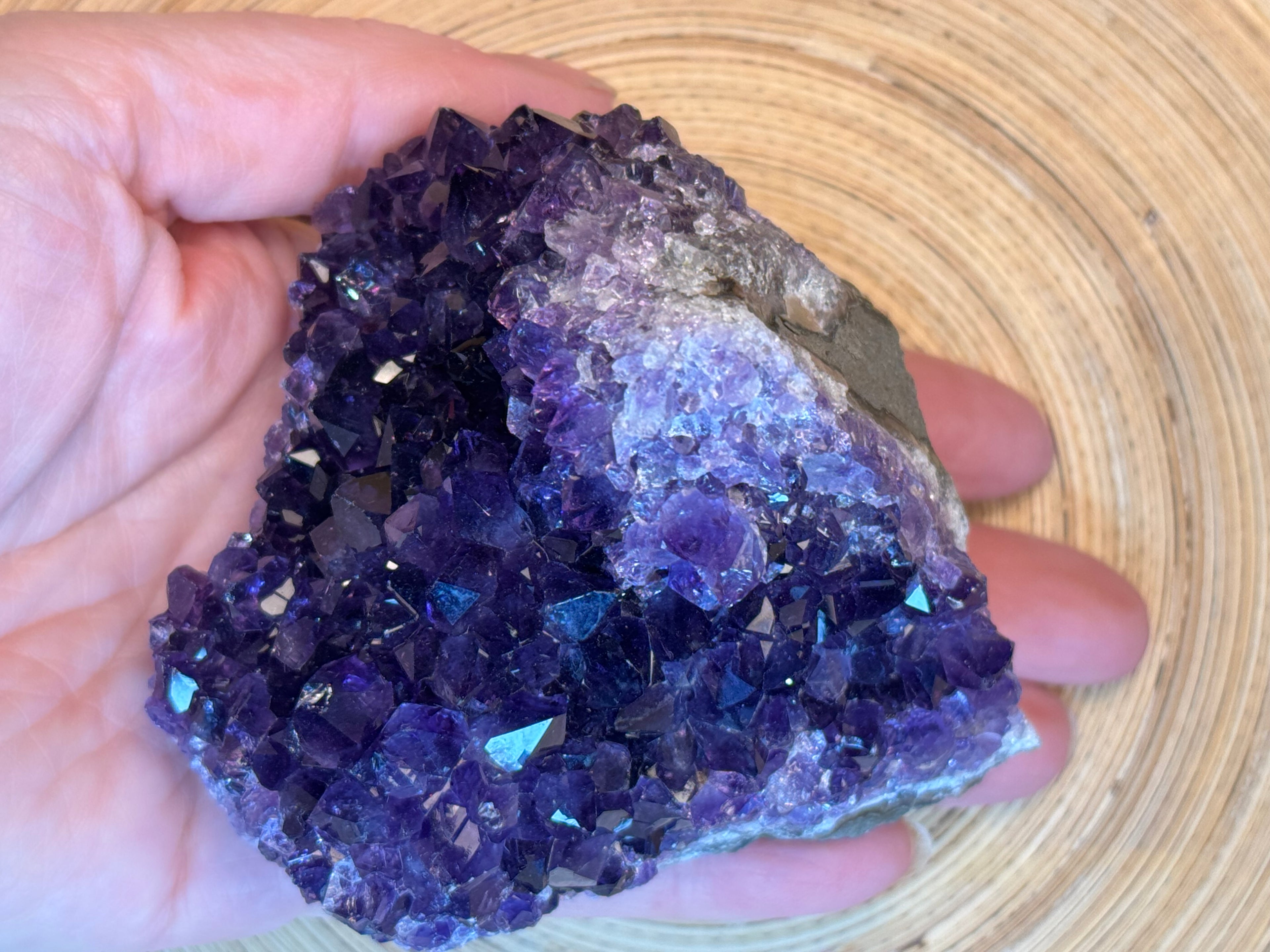 Amethyst crystal cluster held in a hand against a woven mat background
