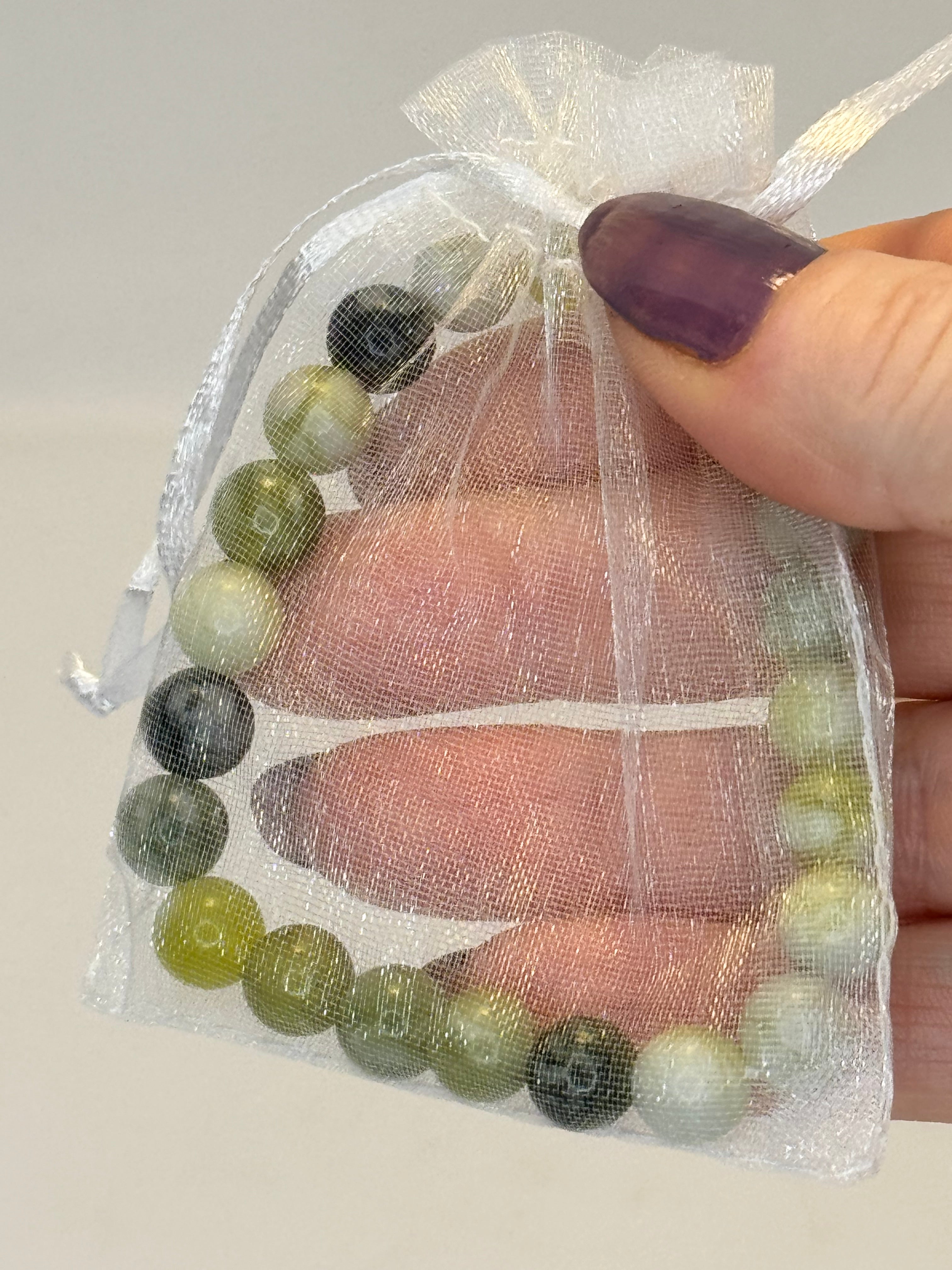 Hand holding a beaded bracelet with green and black beads in a clear plastic bag.
