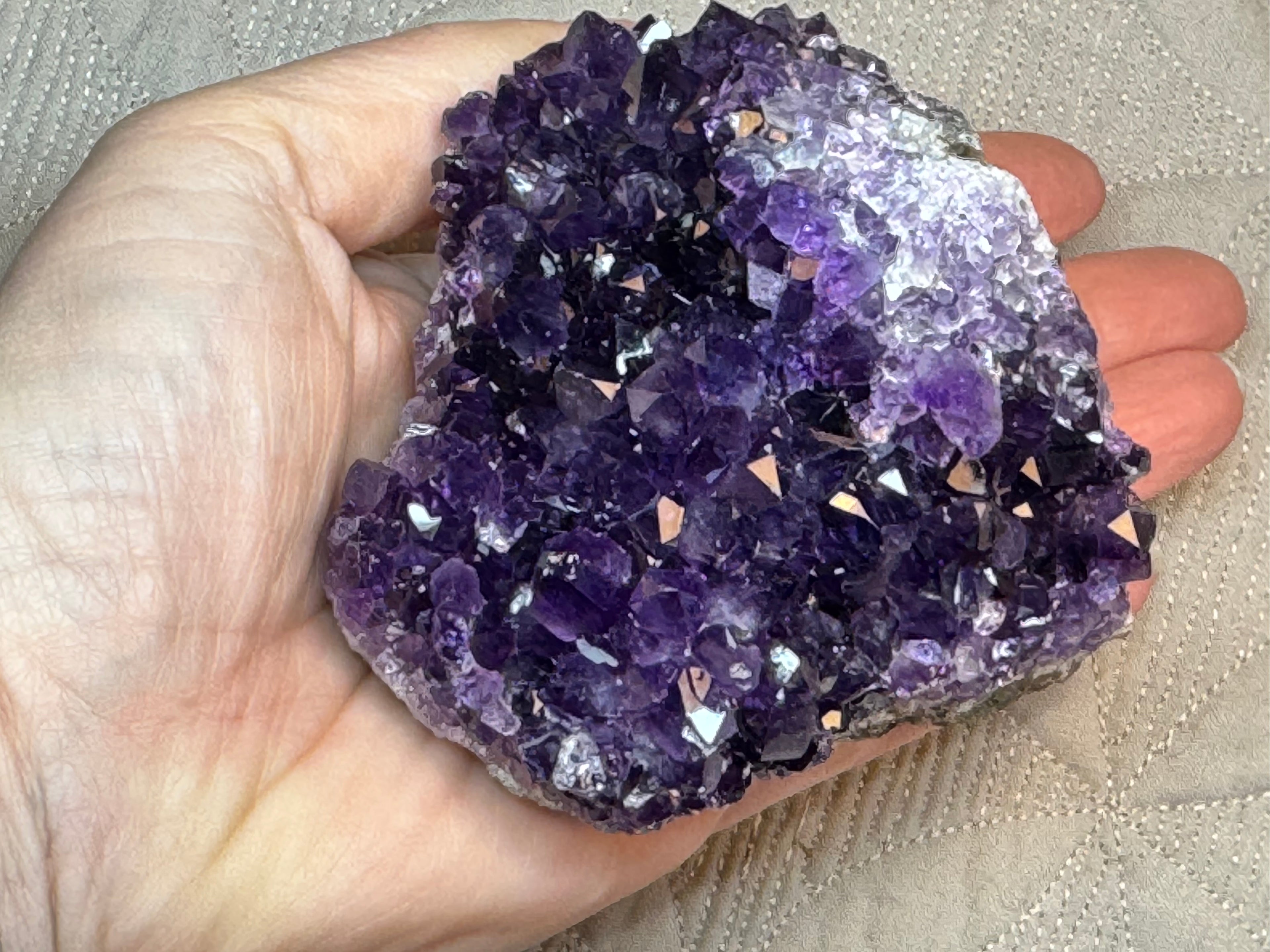 Amethyst crystal cluster held in a hand against a neutral background