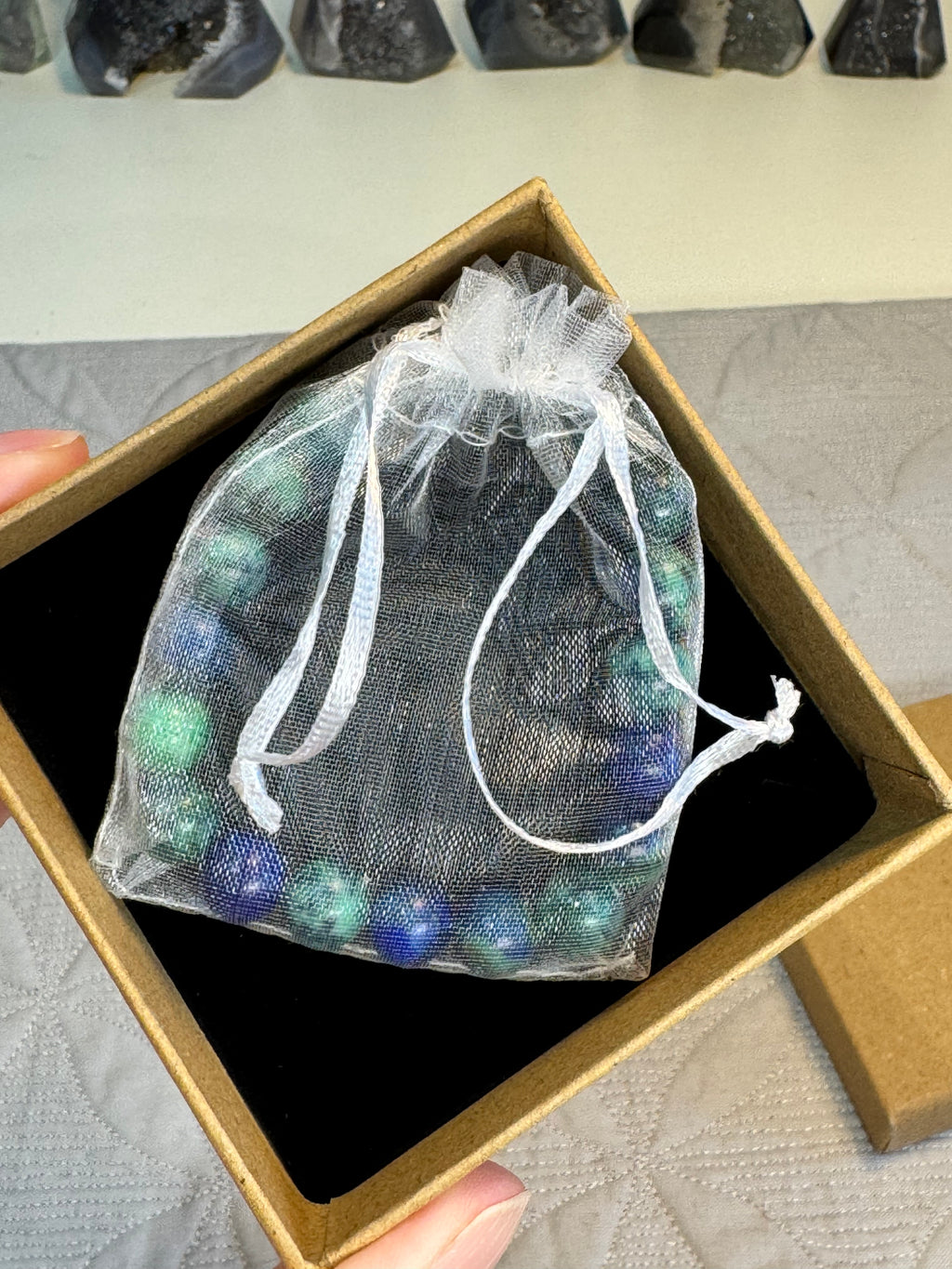 Bag of multicolored stones in a clear drawstring bag inside an open cardboard box.