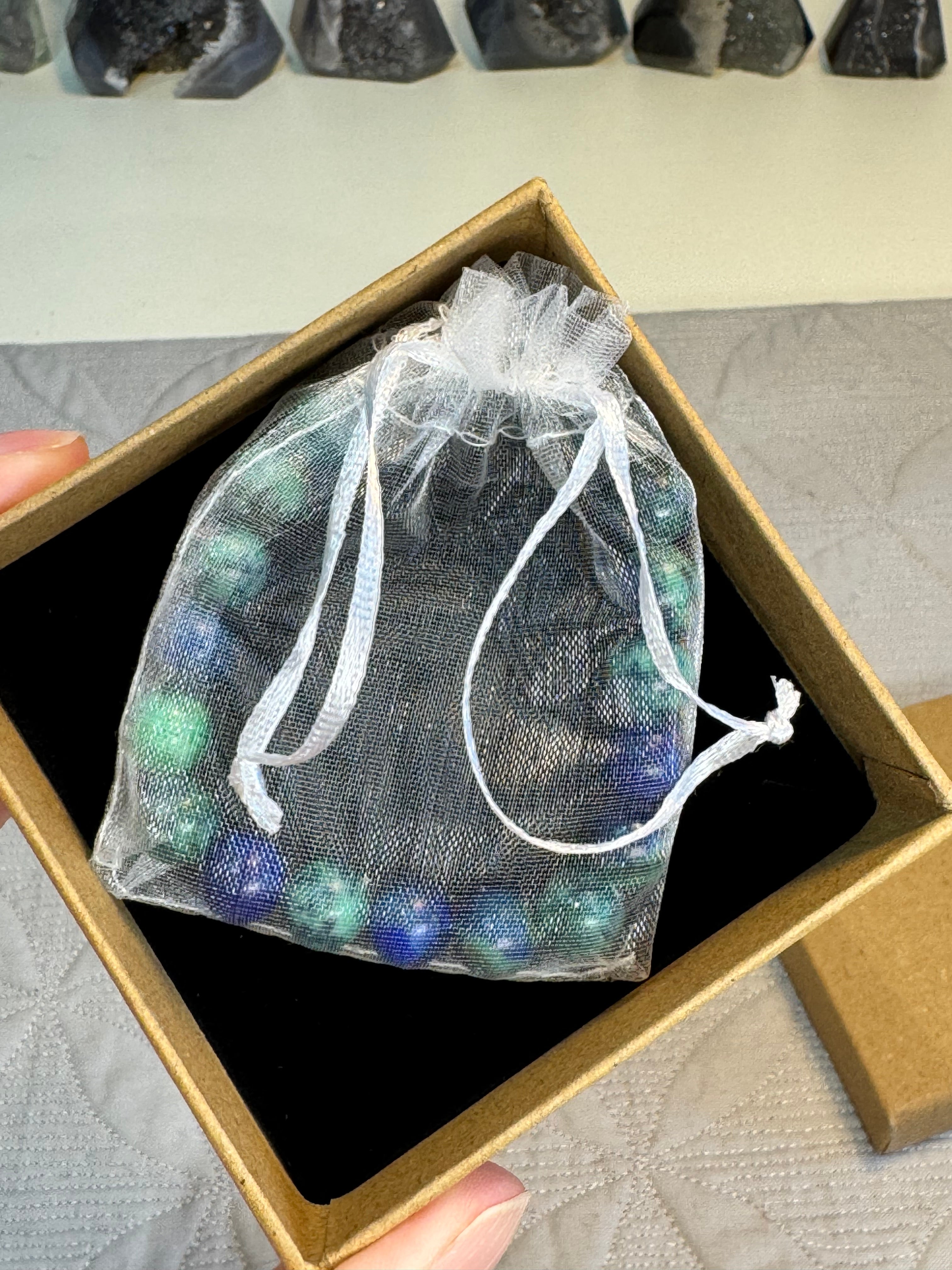 Bag of multicolored stones in a clear drawstring bag inside an open cardboard box.