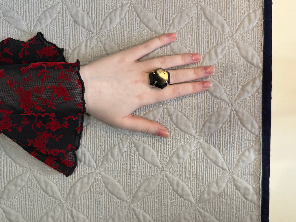 Hand wearing a black and red sleeve with a gold ring on a textured beige surface