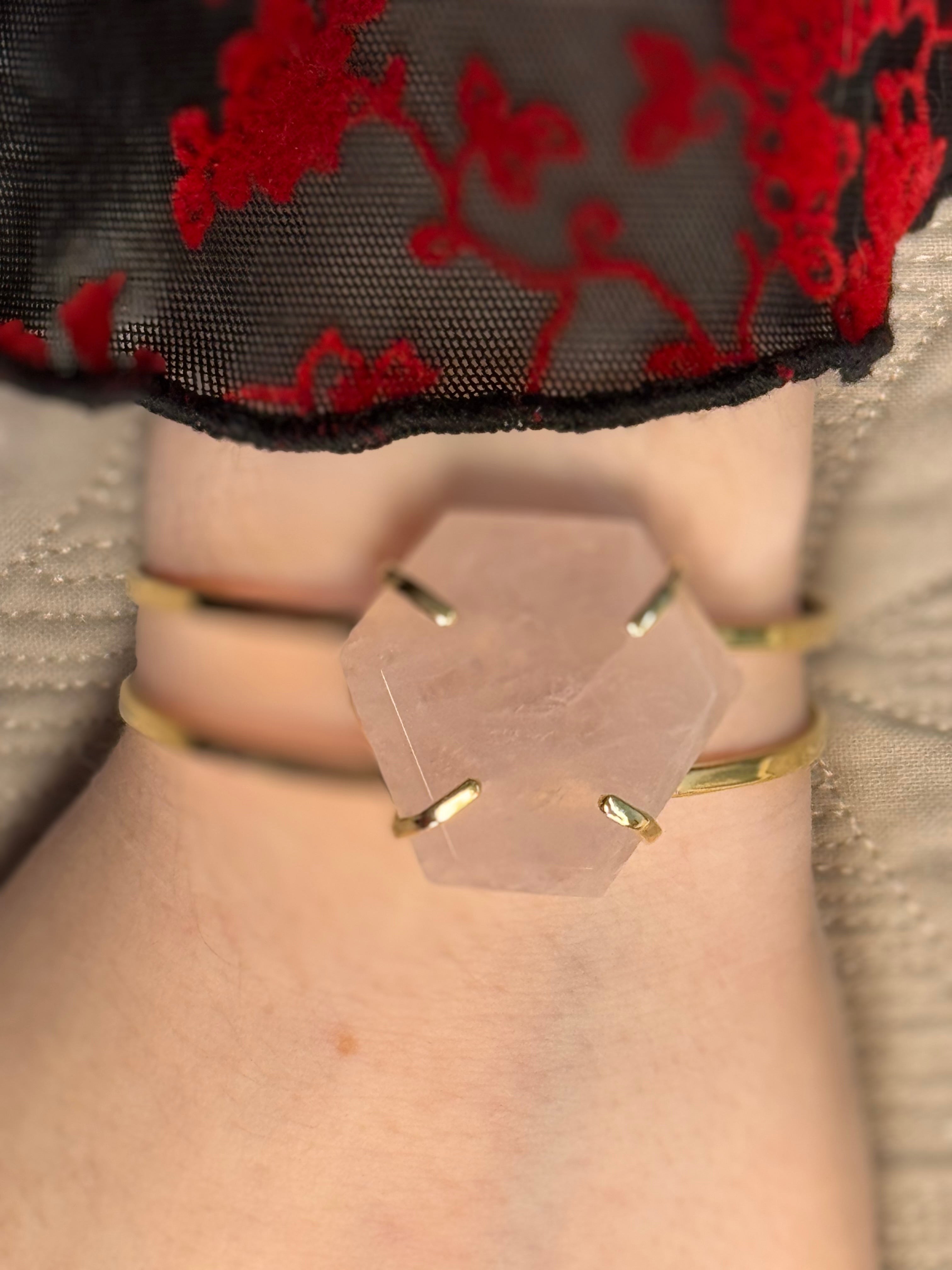 Close-up of a hand wearing a gold bracelet with a clear hexagonal crystal on a neutral background.