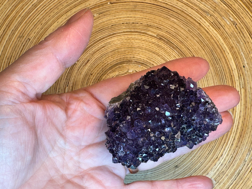 Hand holding a dark purple crystal cluster against a wooden background