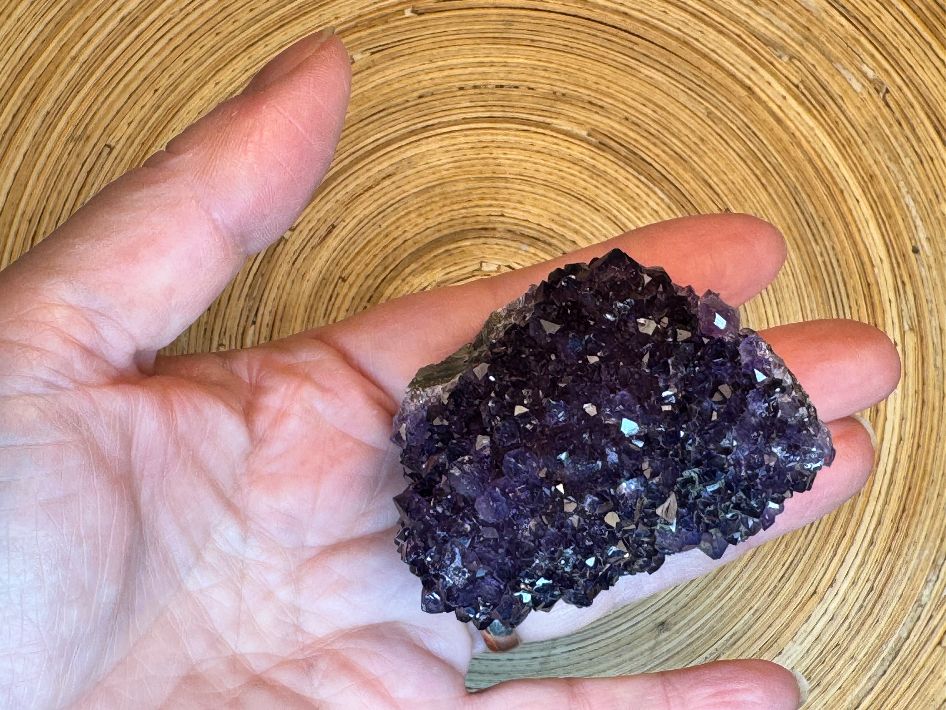 Hand holding a dark purple crystal cluster against a wooden background