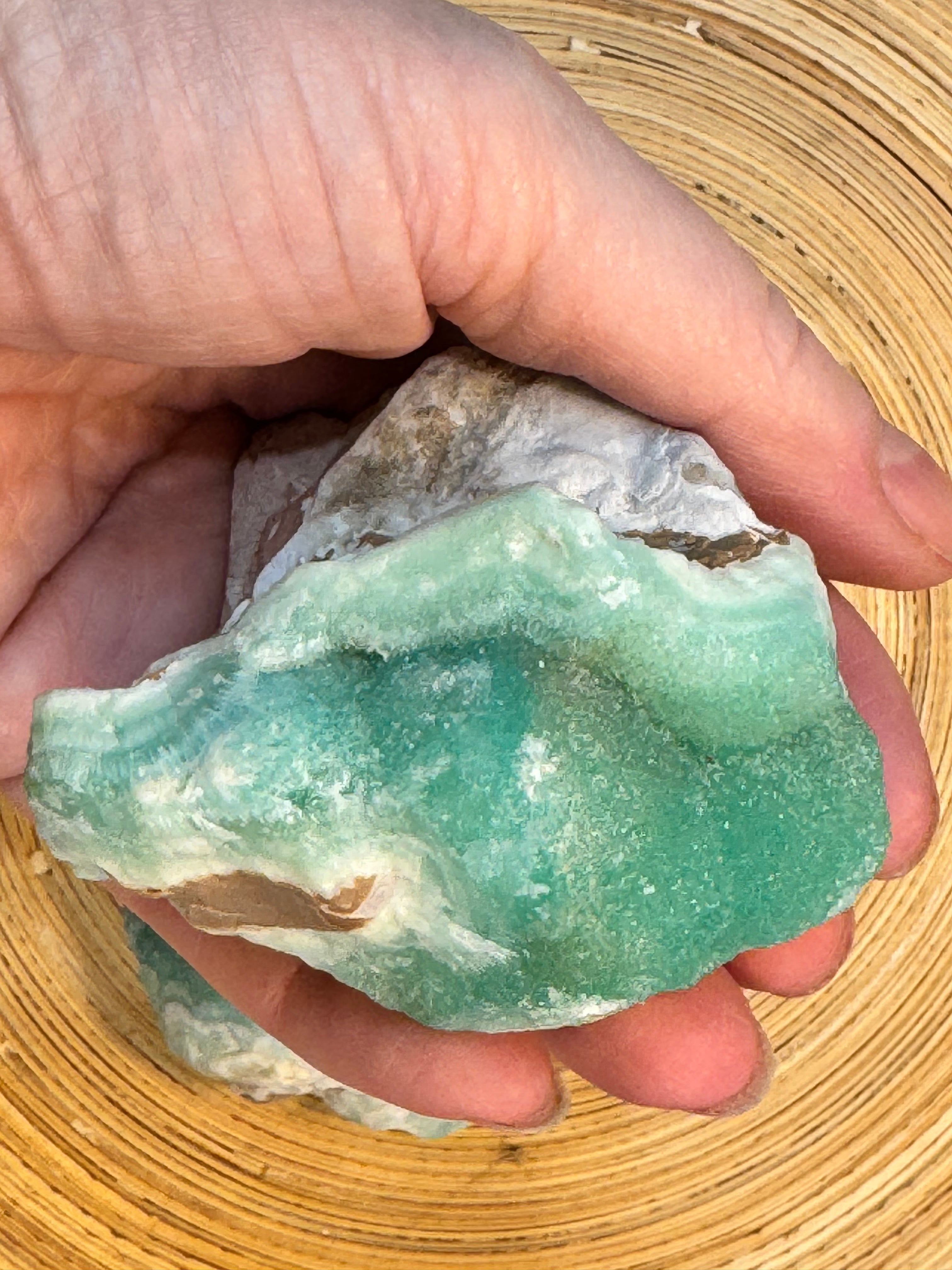 Hand holding a green mineral stone against a woven background