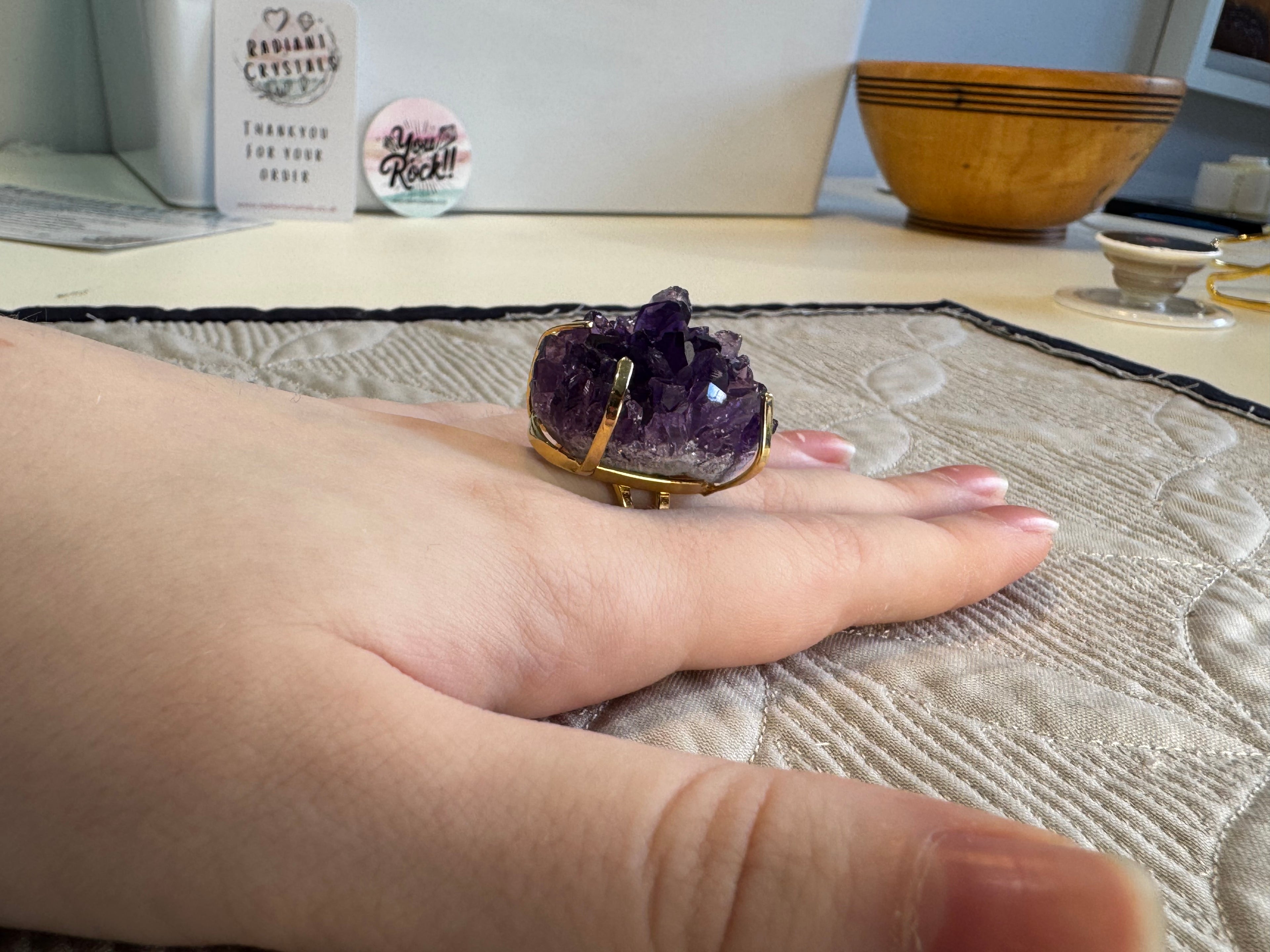Hand wearing a ring with a purple crystal on a textured surface