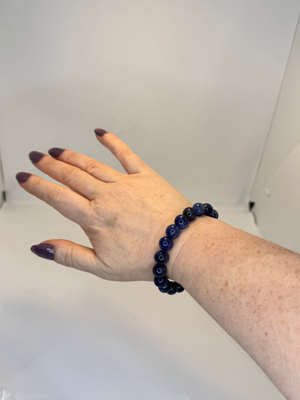 Hand wearing a dark blue beaded bracelet against a plain background