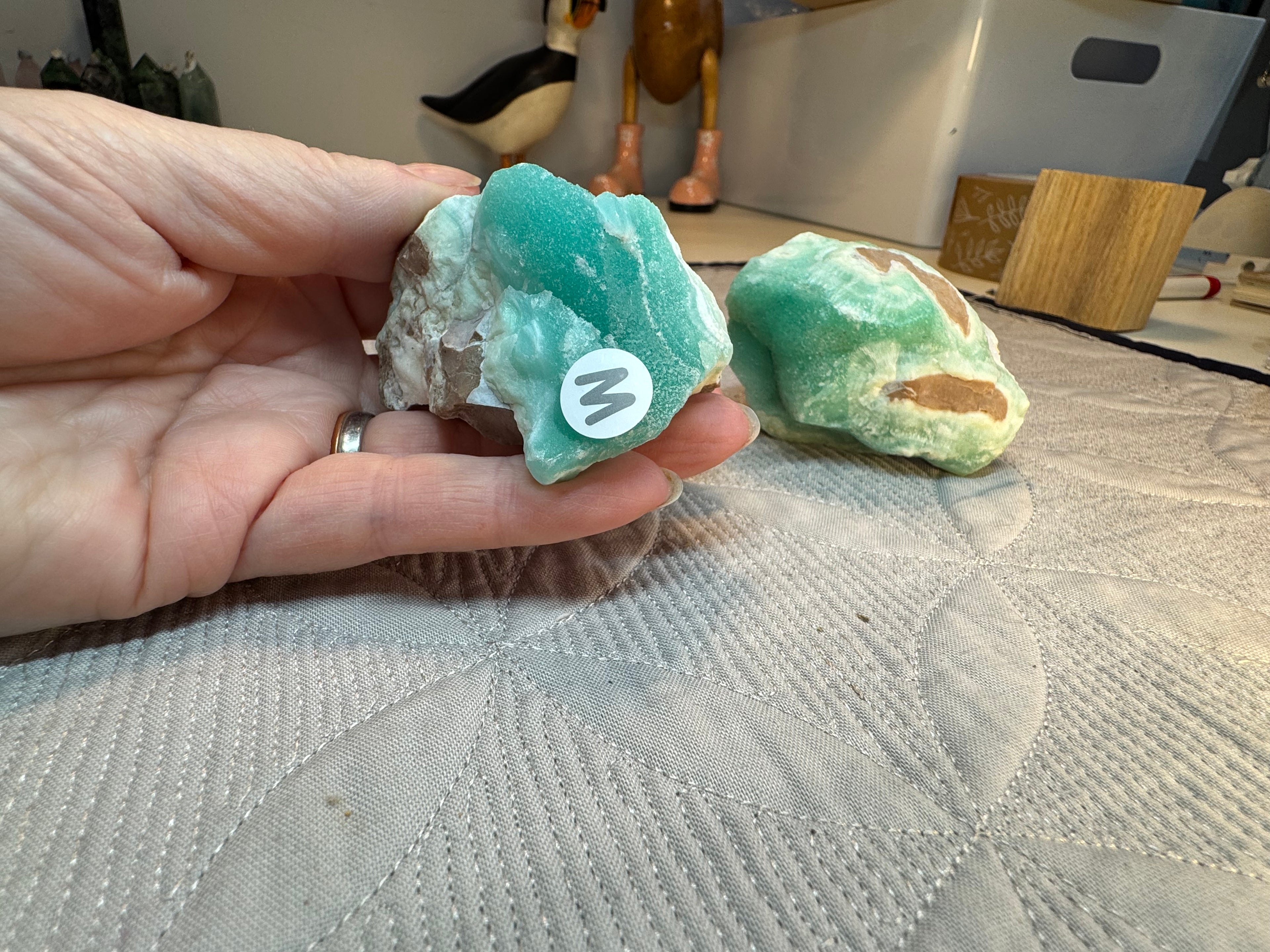 Hand holding a green crystal with a logo, placed on a textured surface.