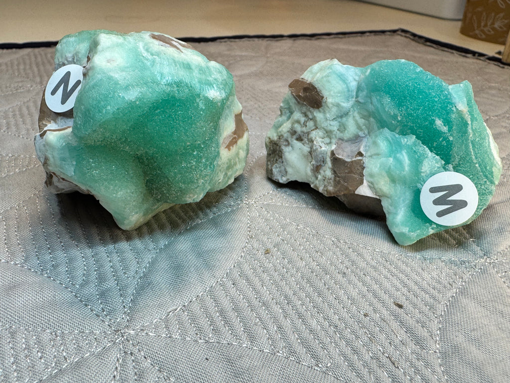 Two green mineral specimens with labels on a textured surface