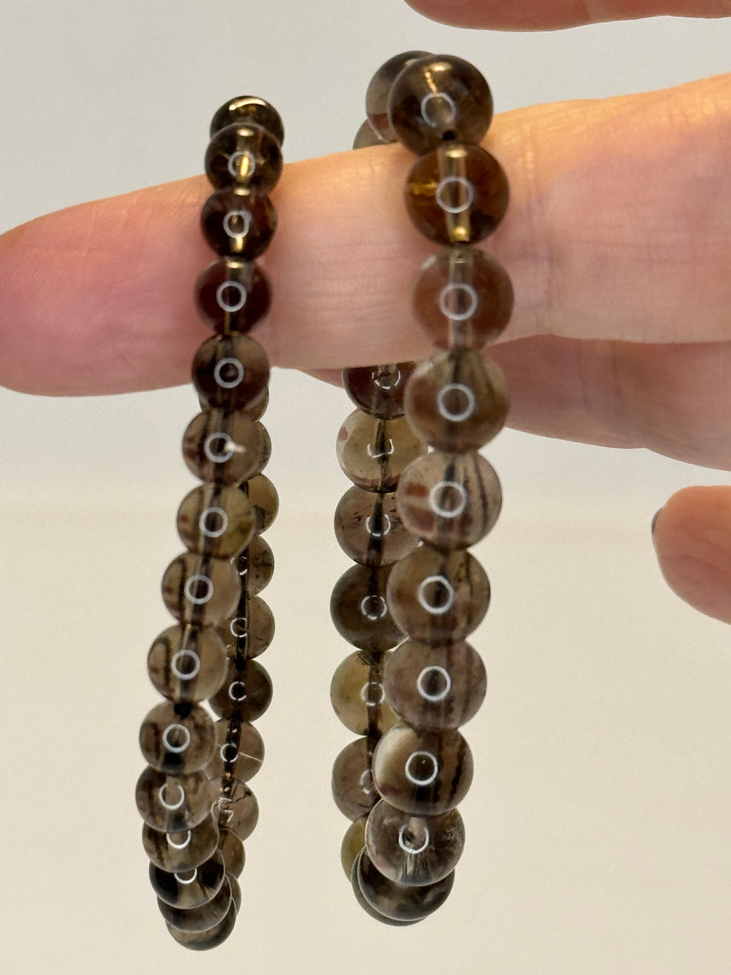 Close-up of a hand holding two brown beaded bracelets against a plain background