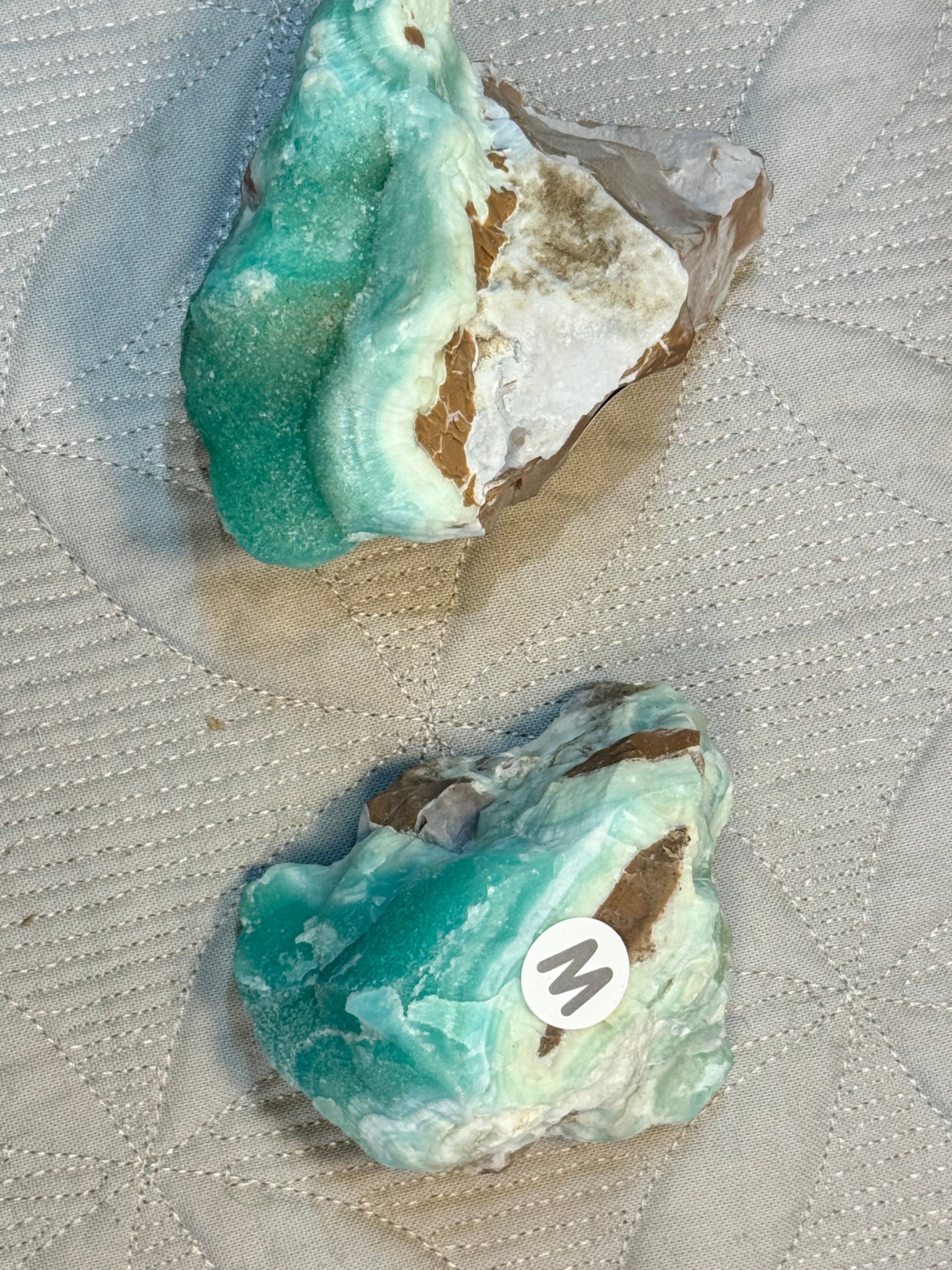 Two turquoise-colored rocks on a textured fabric background