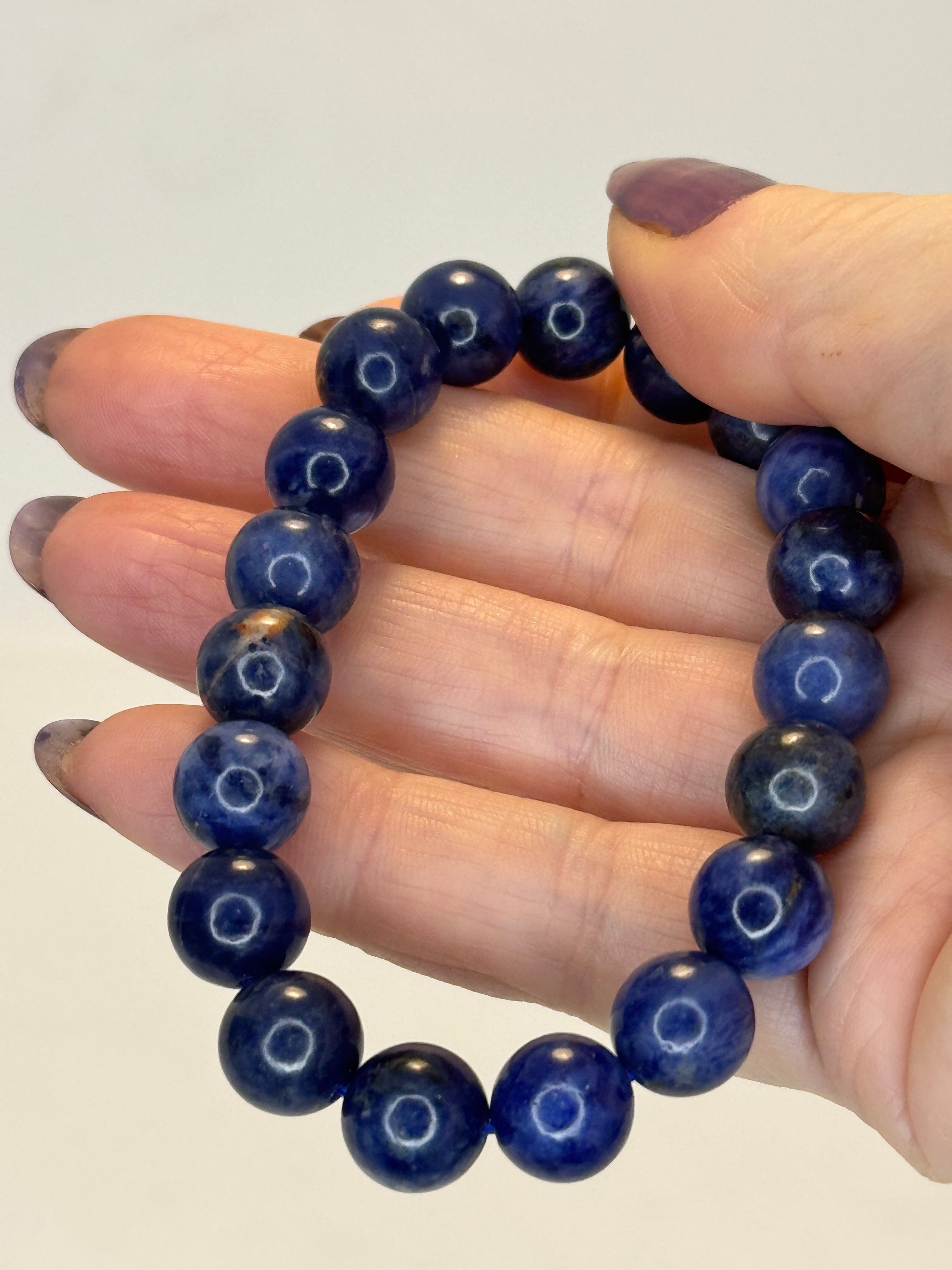Hand wearing a blue beaded bracelet on a plain background