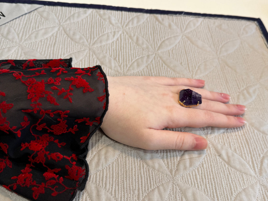 Hand wearing a dark purple gemstone ring on a textured surface