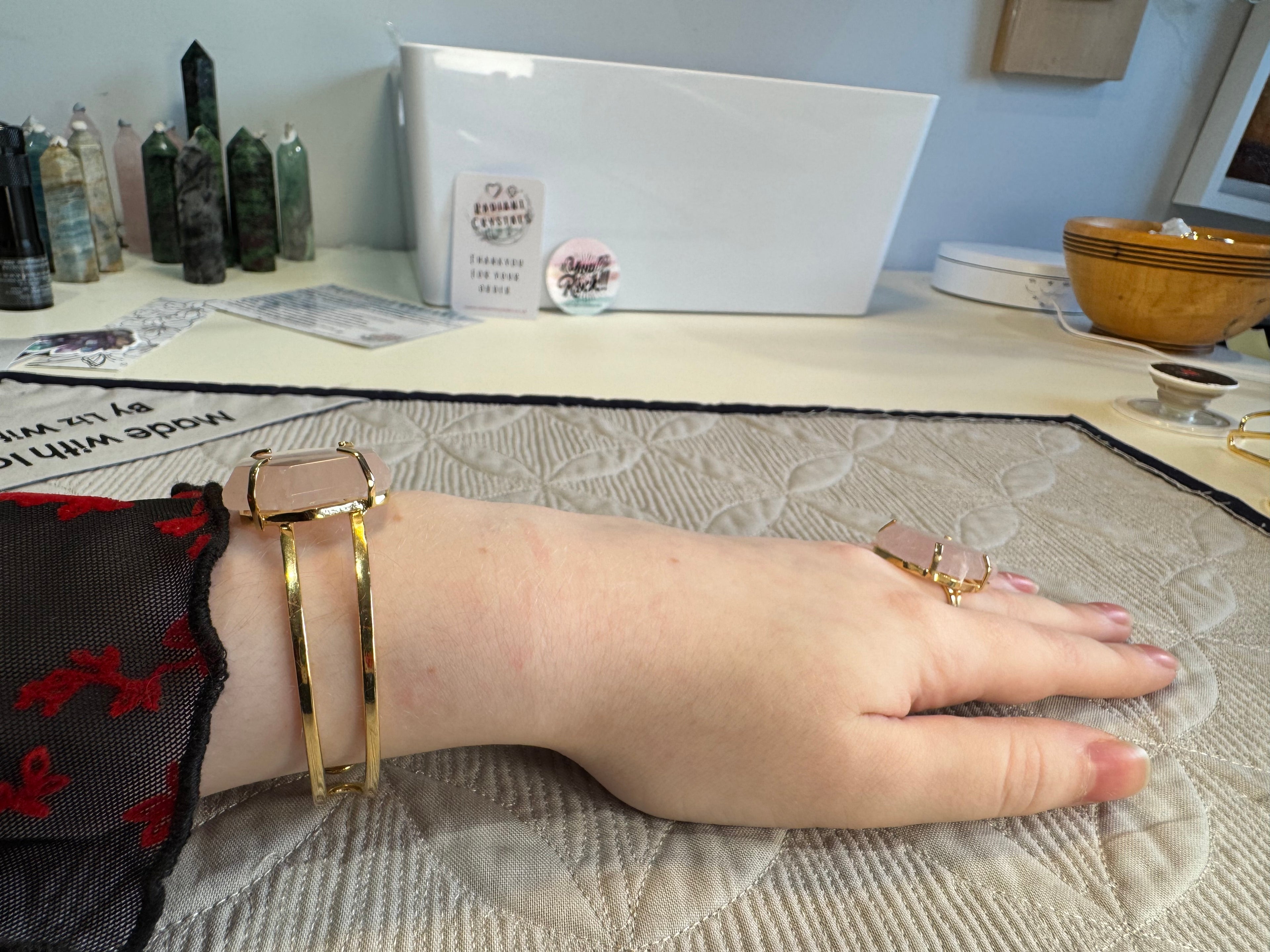 Hand wearing a gold bracelet and ring on a textured surface with a blurred background