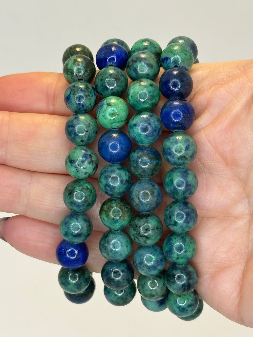 Stack of green and blue beaded bracelets held in a hand against a neutral background