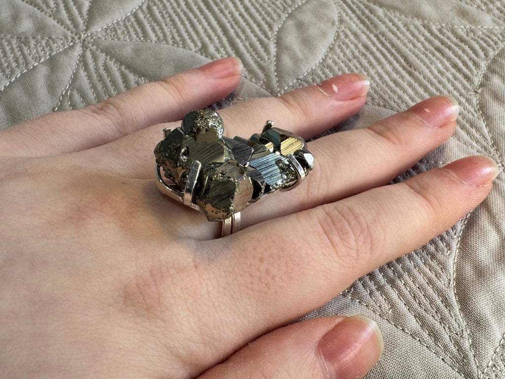 Hand wearing a decorative ring with pyrite stones on a textured fabric background
