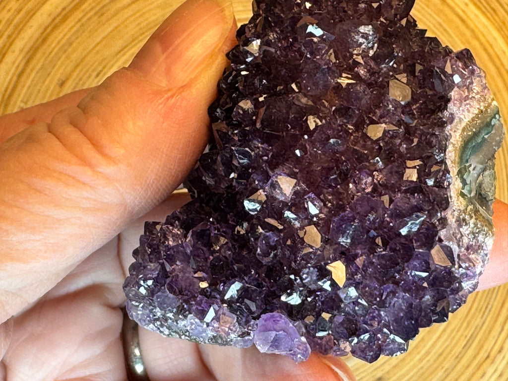 Amethyst crystal cluster held in a hand against a wooden background