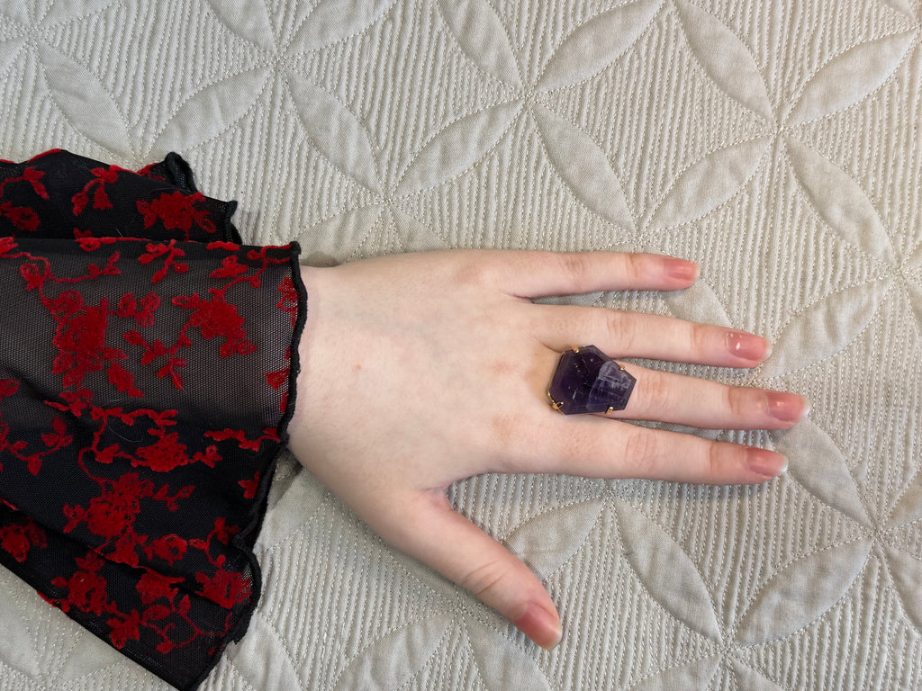 Hand wearing a purple Amethyst ring on a textured beige surface