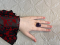 Hand wearing a purple Amethyst ring on a textured beige surface
