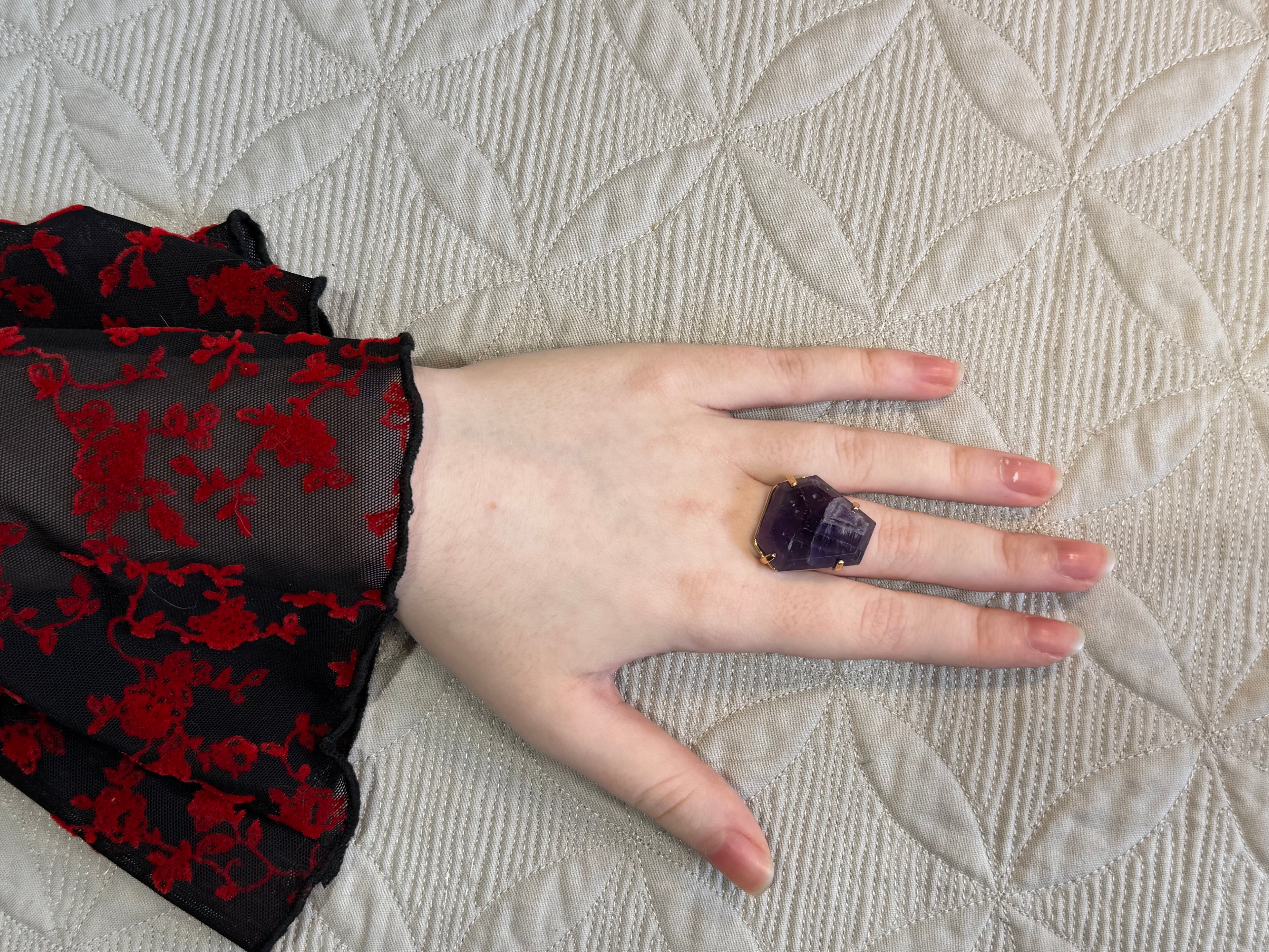 Hand wearing a purple Amethyst ring on a textured beige surface