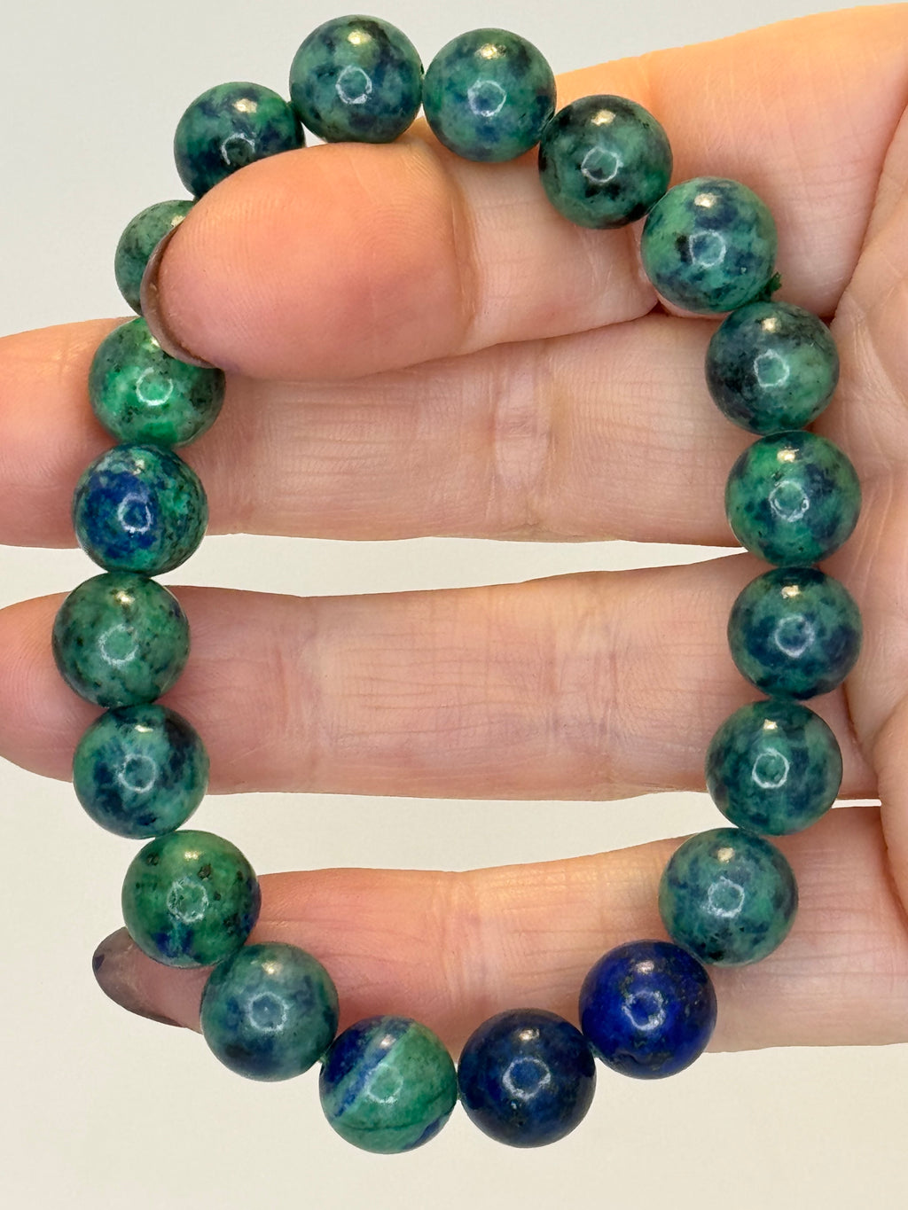 Green and blue beaded bracelet on a hand against a plain background
