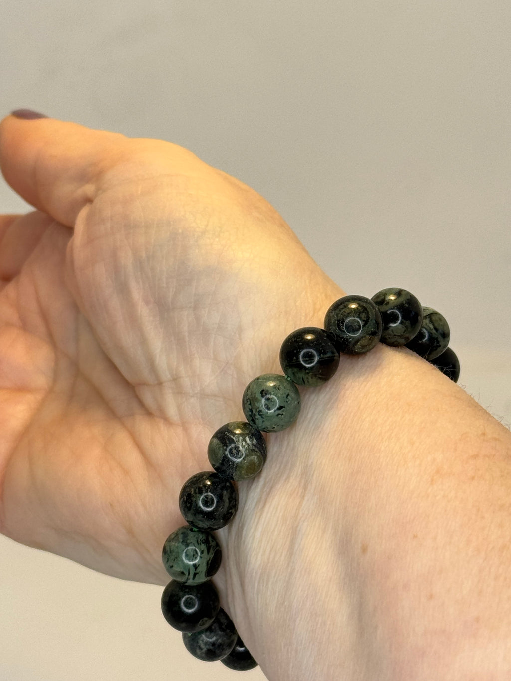 Hand wearing a bracelet with black and green beads on a plain background