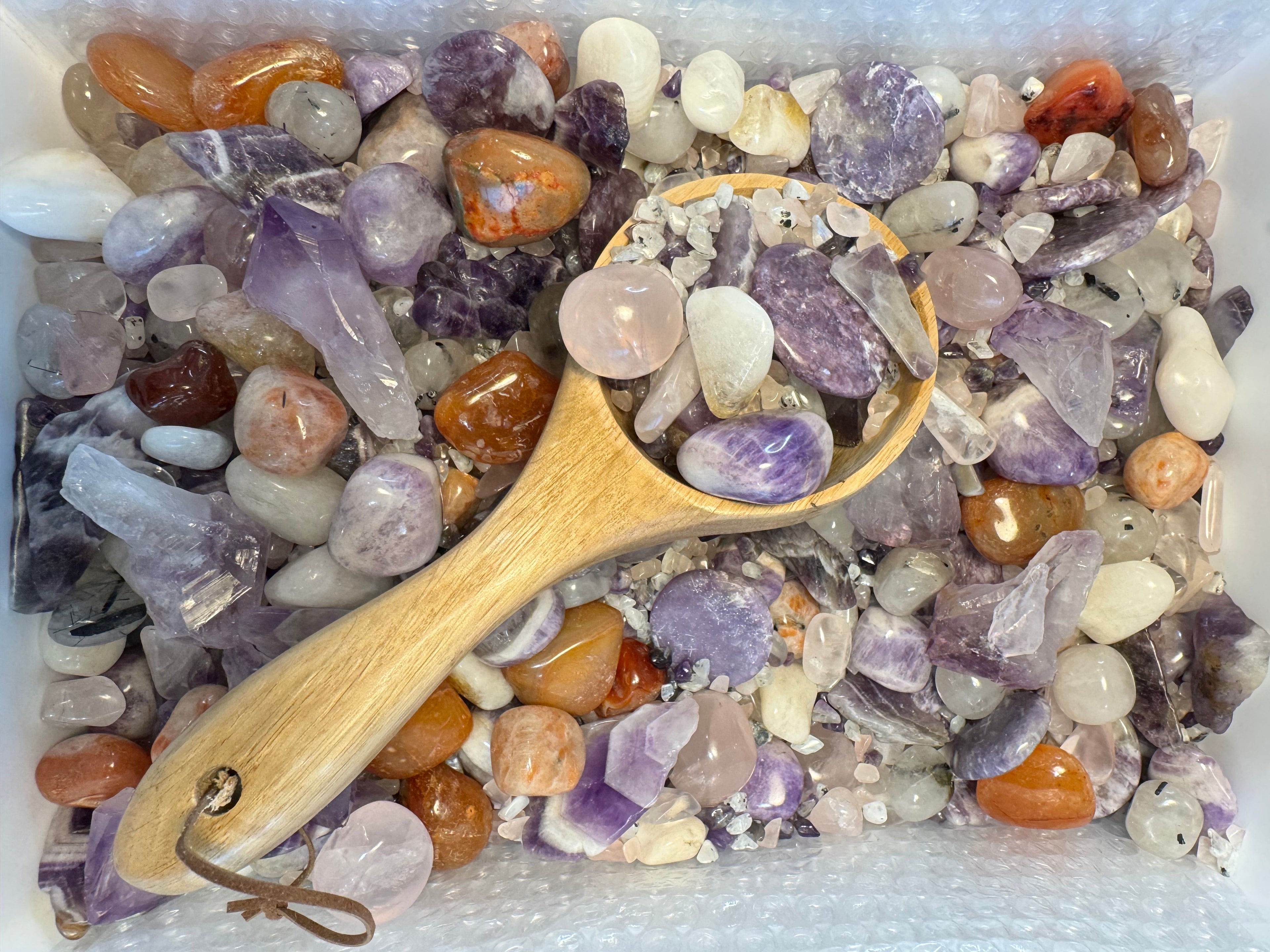 Wooden scoop over a mix of multicolored stones and crystals
