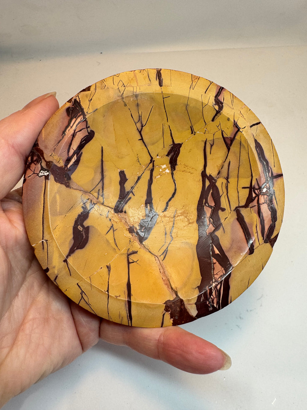 Round decorative plate with a yellow and brown abstract pattern held by a hand against a neutral background