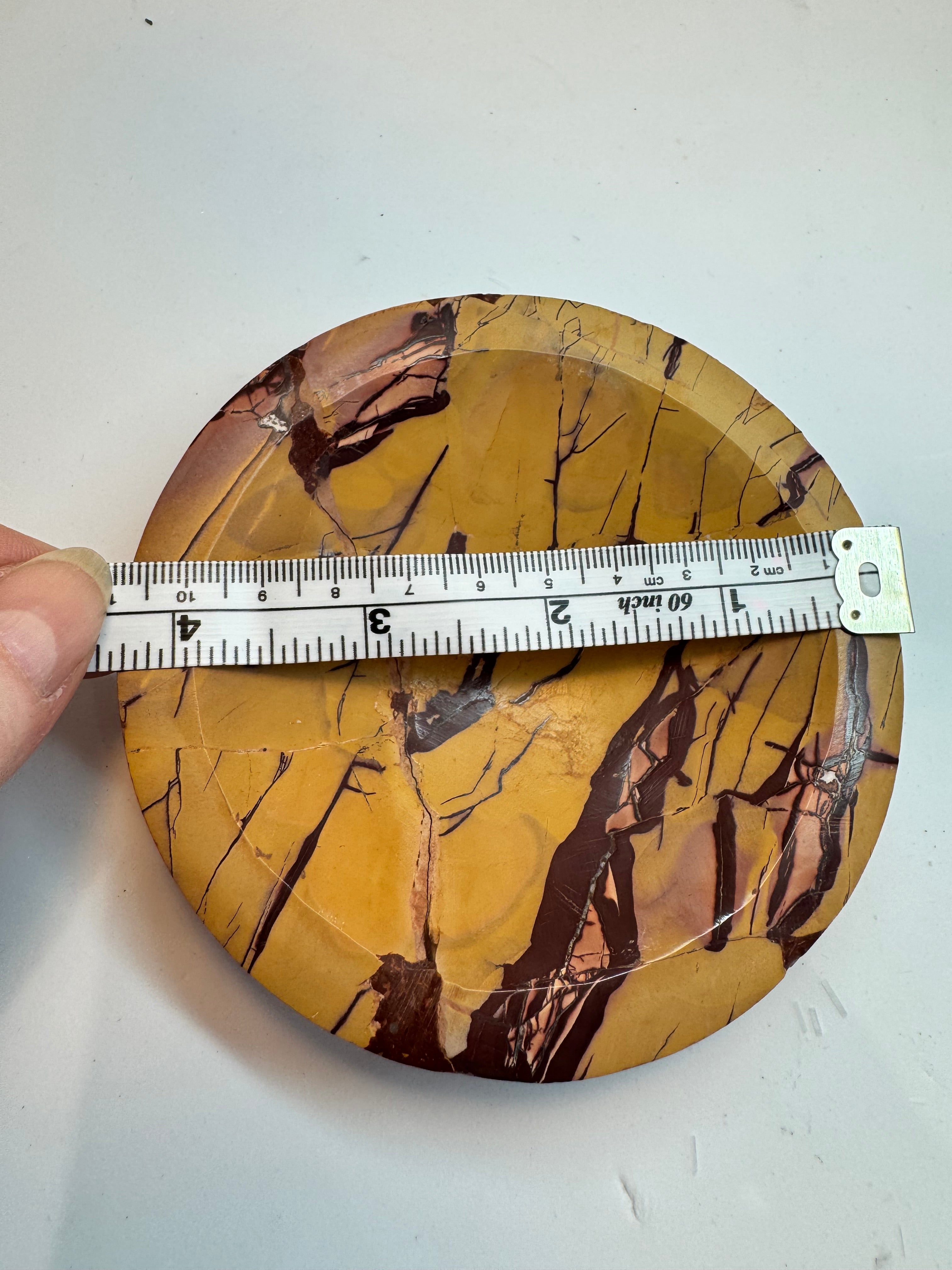 Round stone with marbled pattern held by a hand, with a ruler for scale on a white background