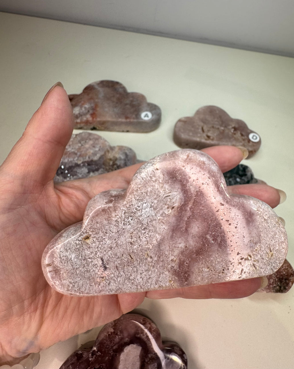 Hand holding a cloud-shaped stone with other similar stones in the background on a light surface.