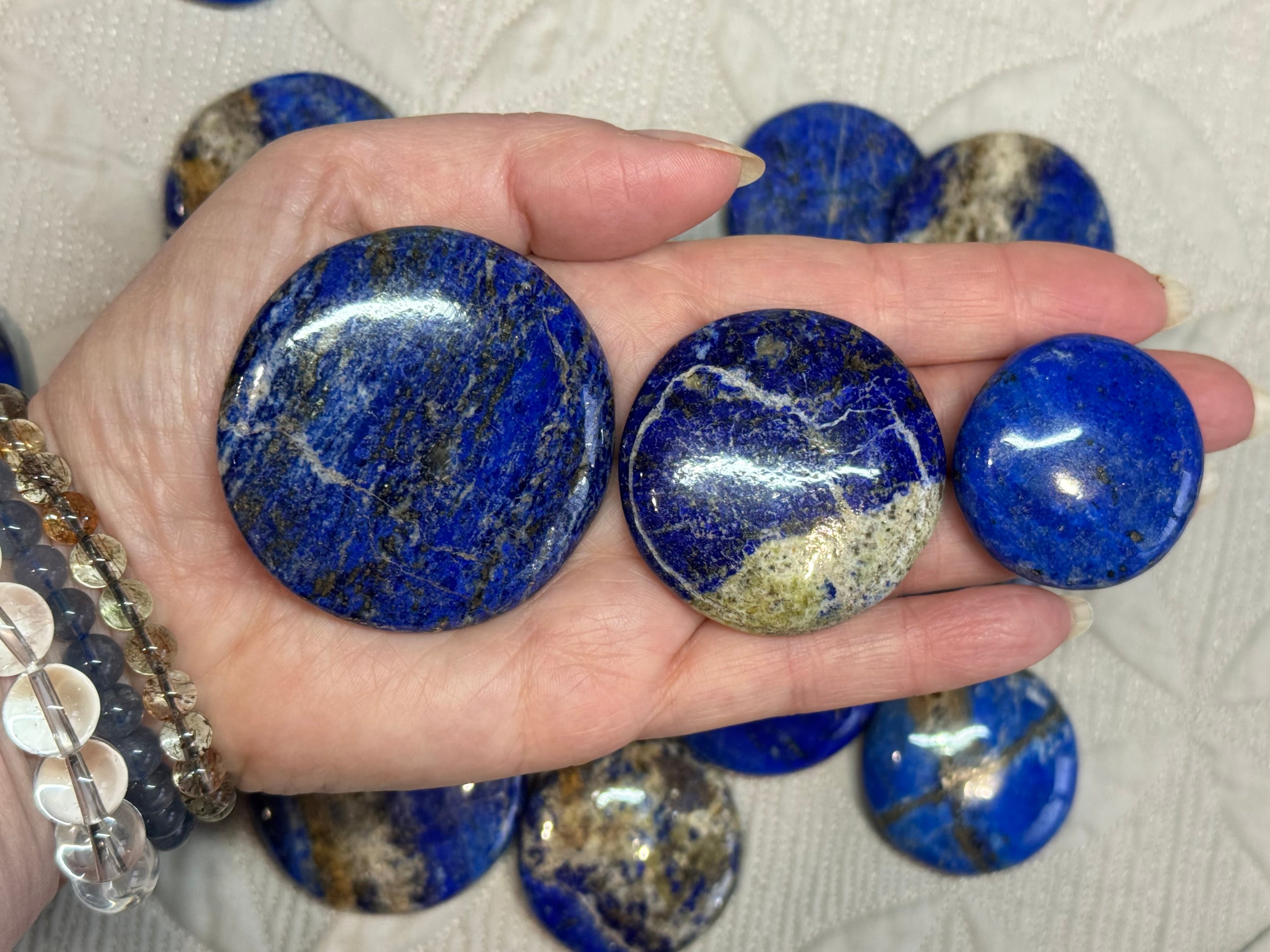 Hand holding three blue marbled stones with more stones in the background on a textured surface.