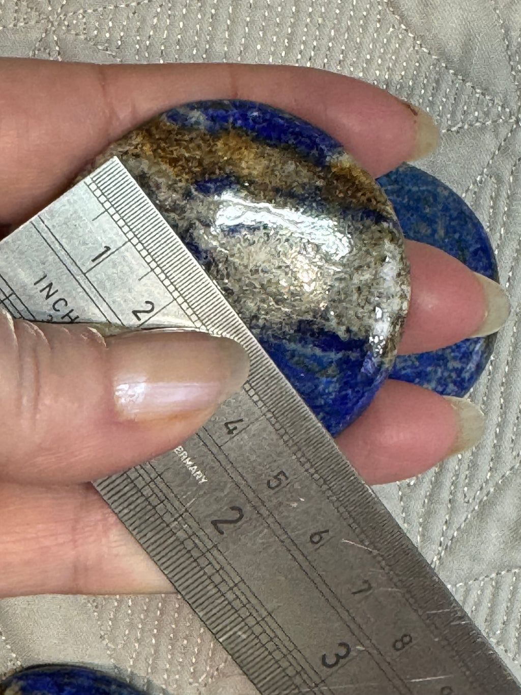Hand holding a lapis lazuli stone with a ruler for scale on a textured fabric background