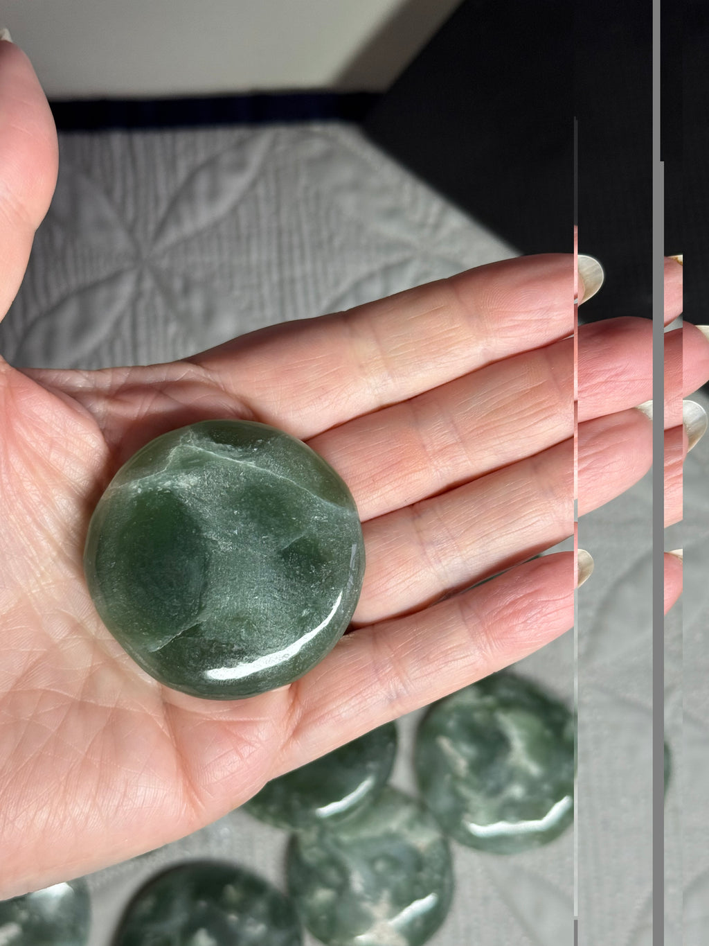 Hand holding a green stone with more stones in the background