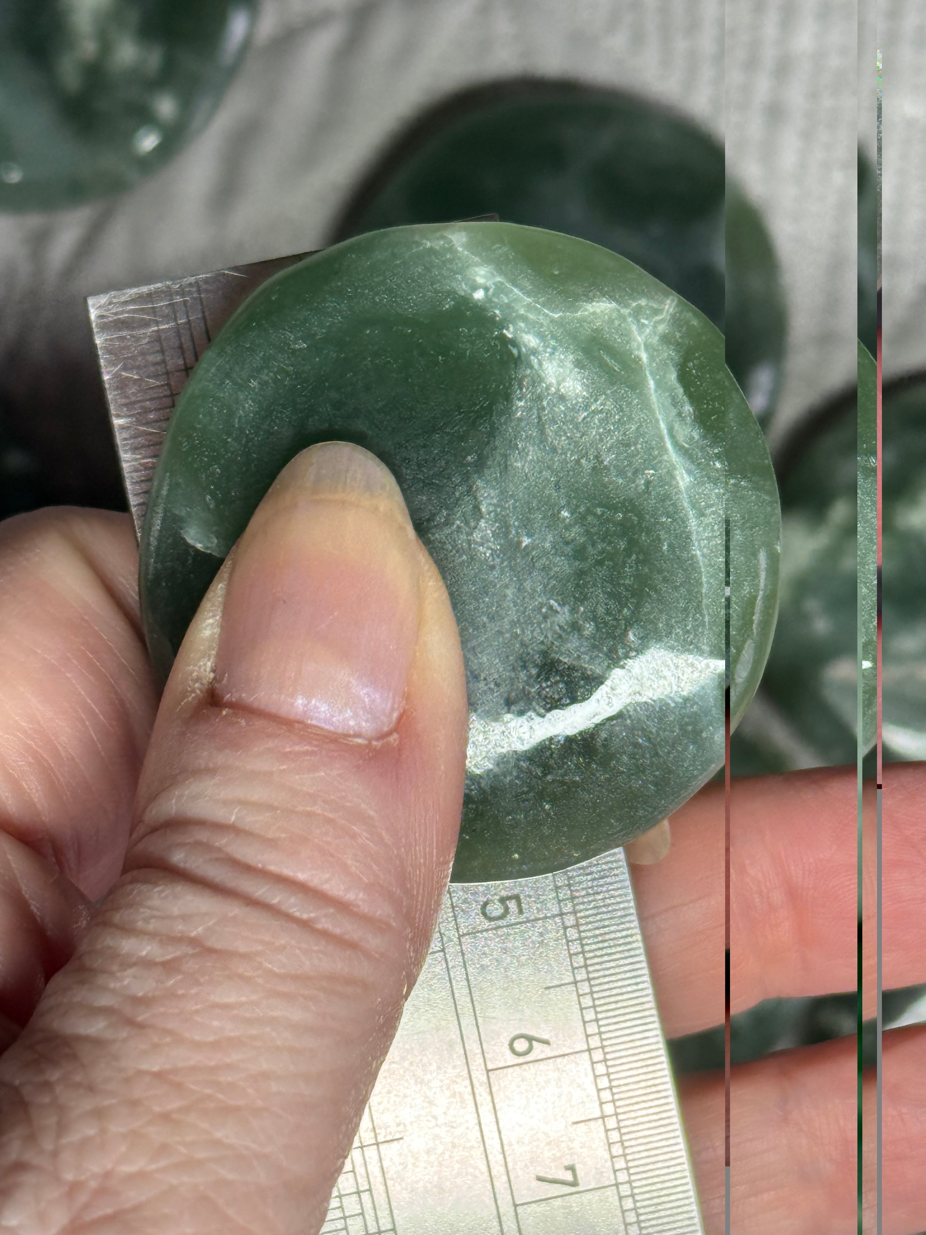 Green stone held by a hand with a ruler for scale