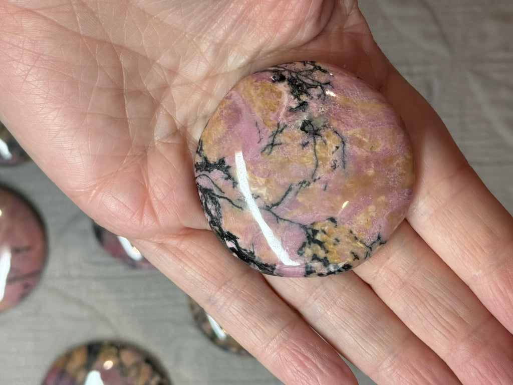 Hand holding a pink and black marbled stone with blurred stones in the background