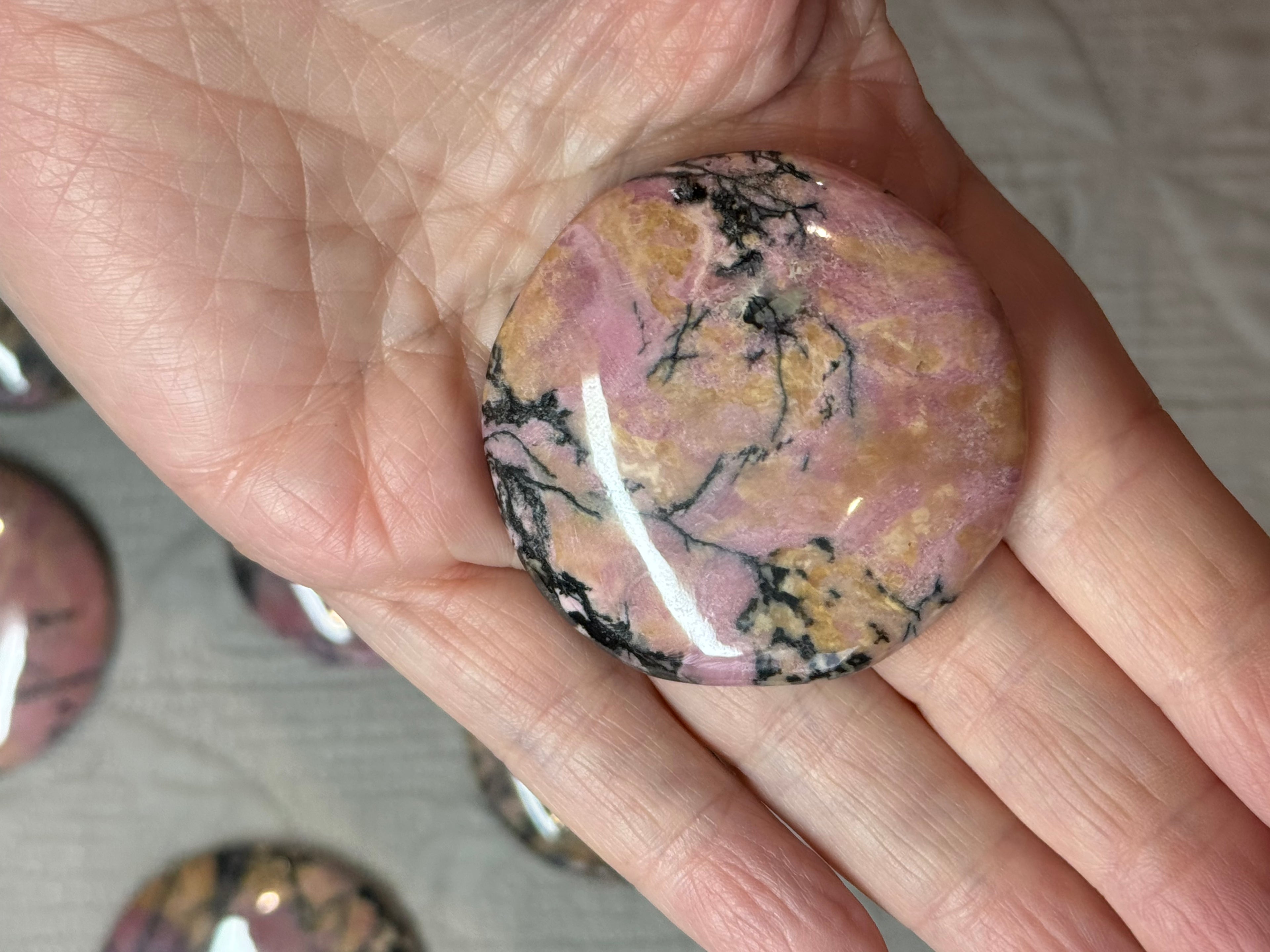 Hand holding a pink and black marbled stone with blurred stones in the background