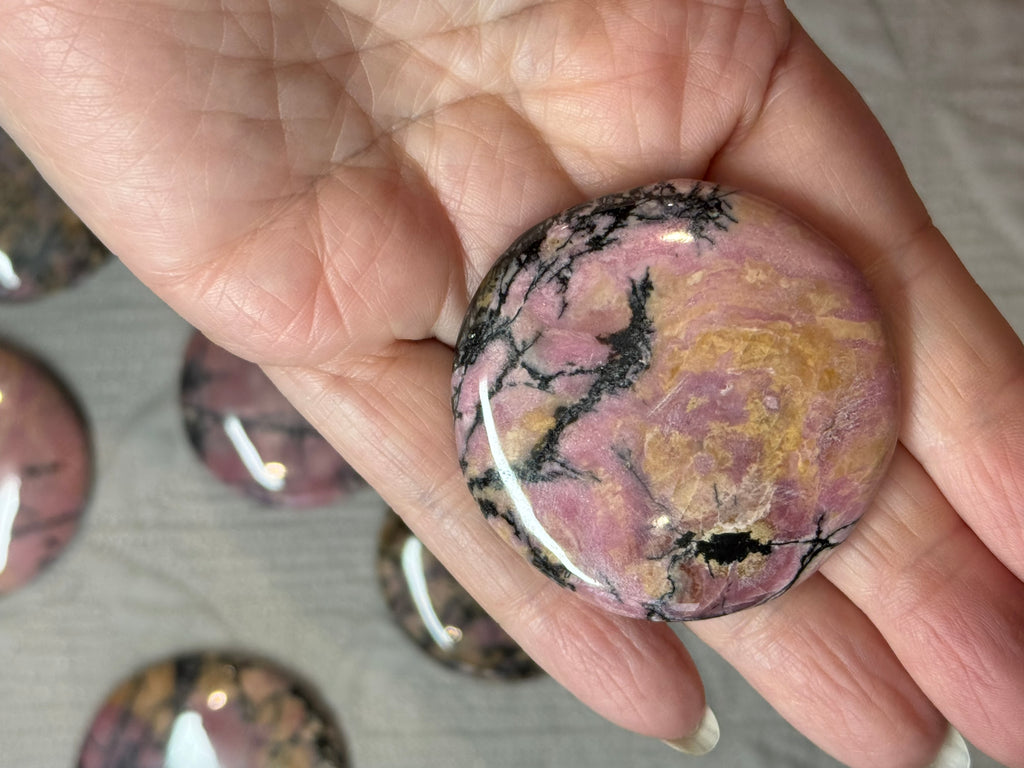 Marbled pink and black stone held in a hand with blurred stones in the background