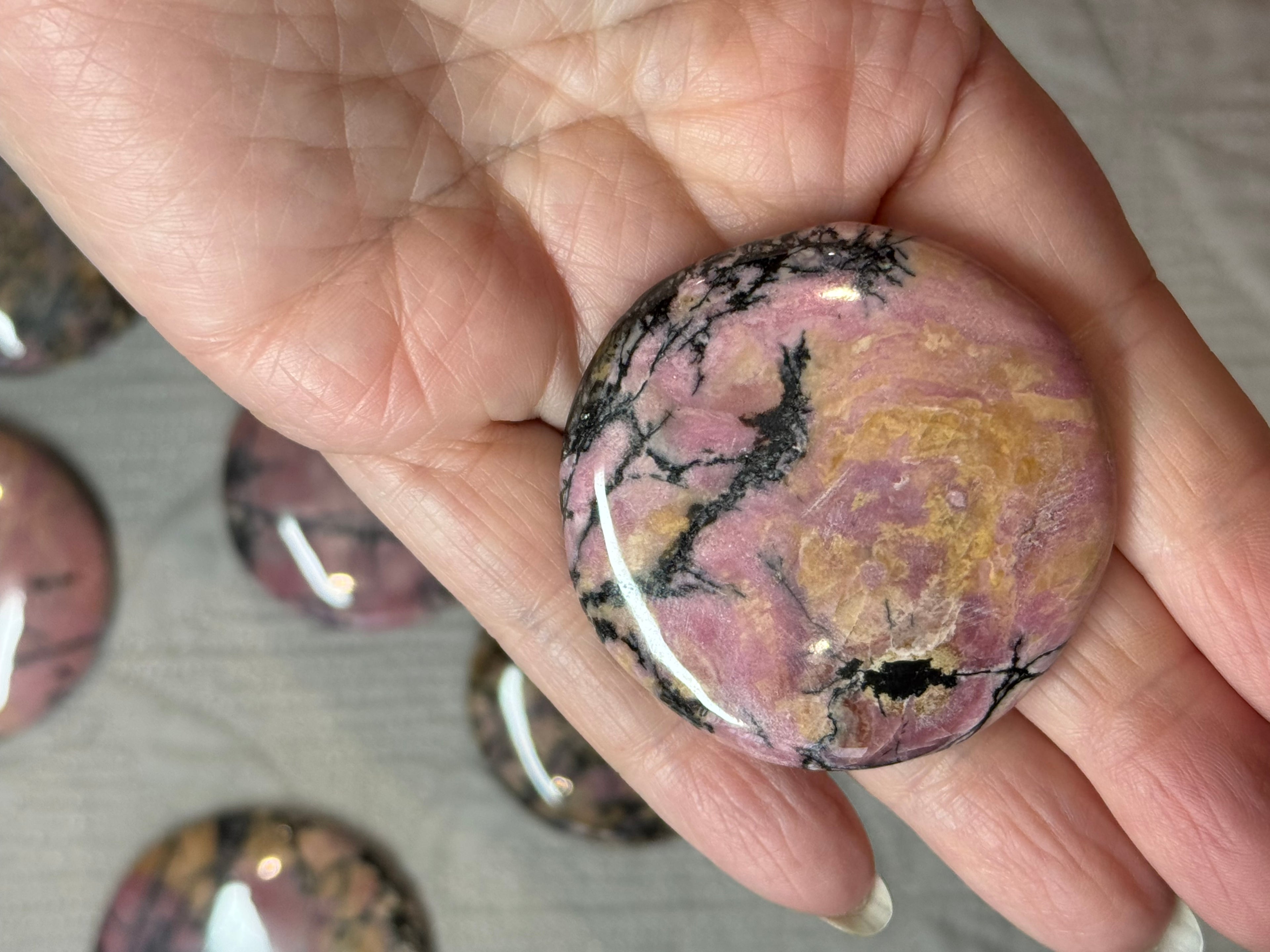 Marbled pink and black stone held in a hand with blurred stones in the background