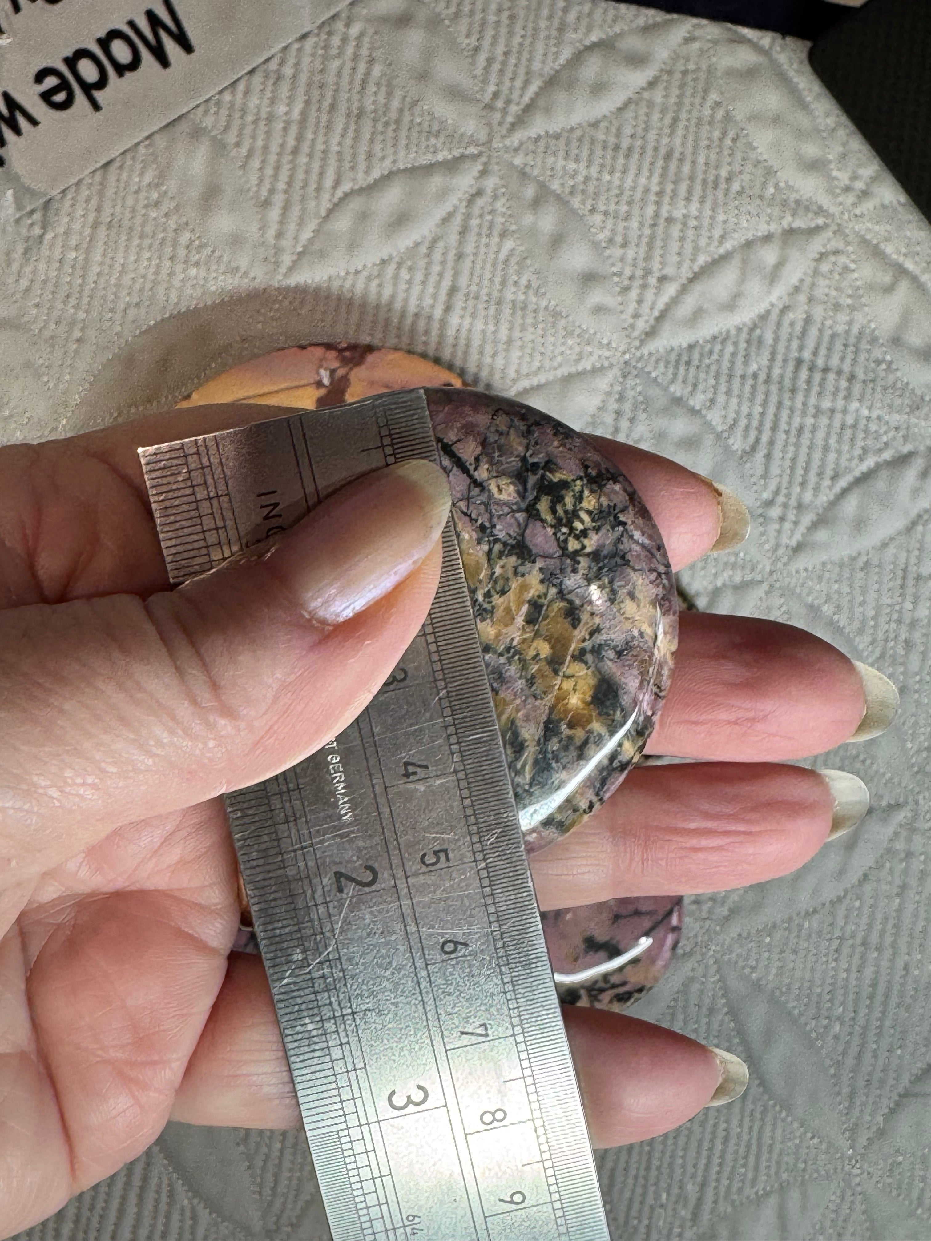 Hand holding a round stone with a ruler for scale against a textured background
