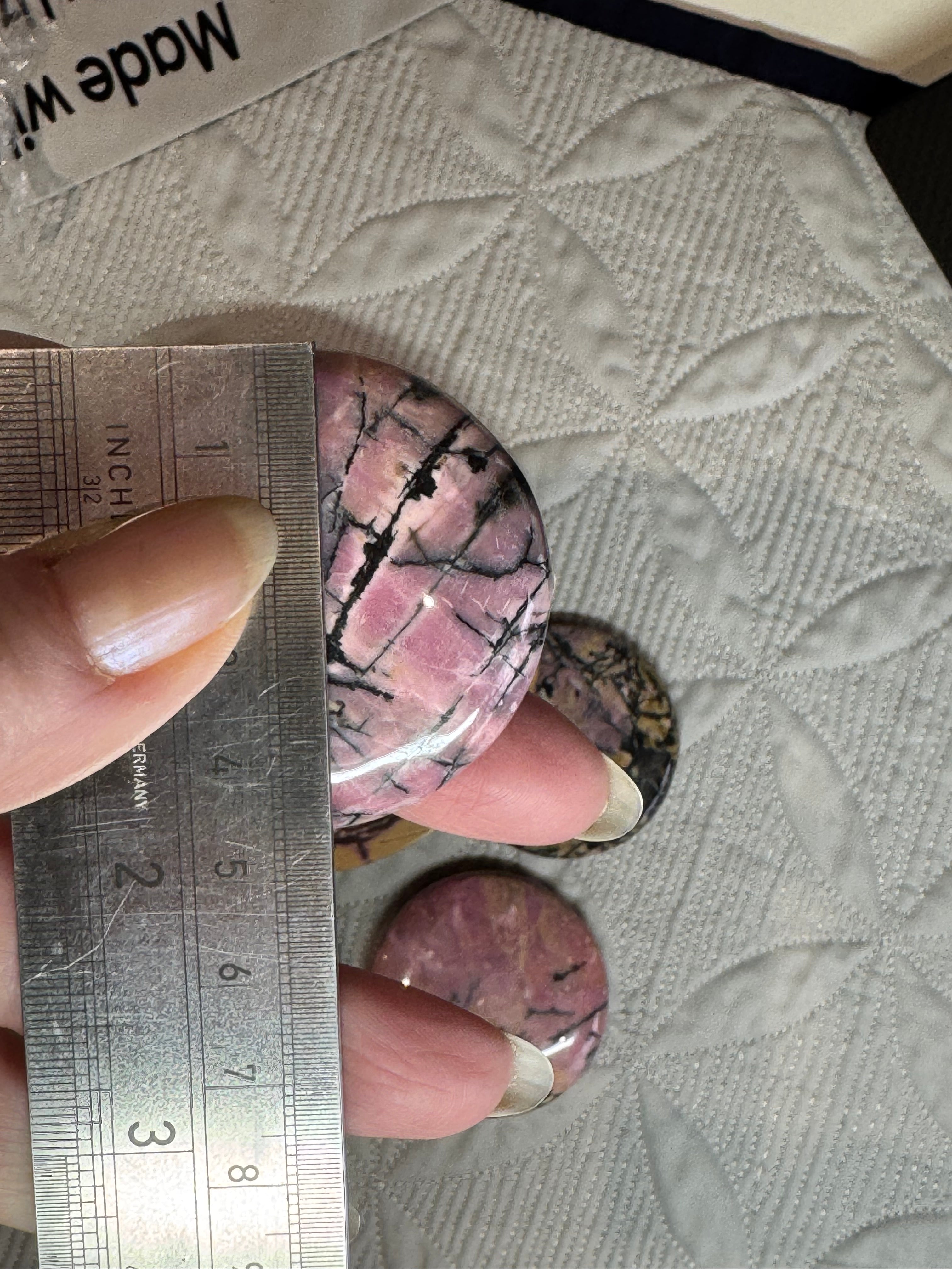 Hand holding a pink stone with a ruler for scale on a textured surface