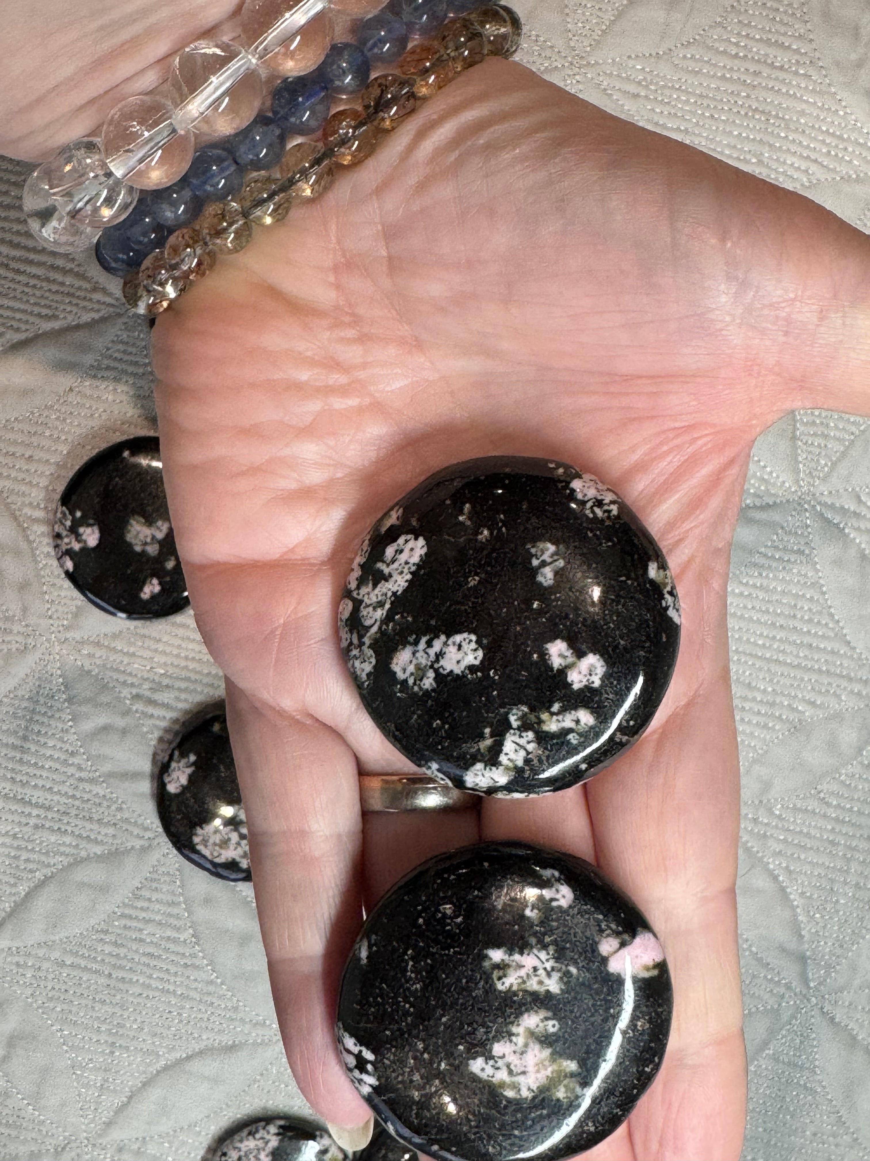 Black stones with white specks held in a hand against a textured gray background