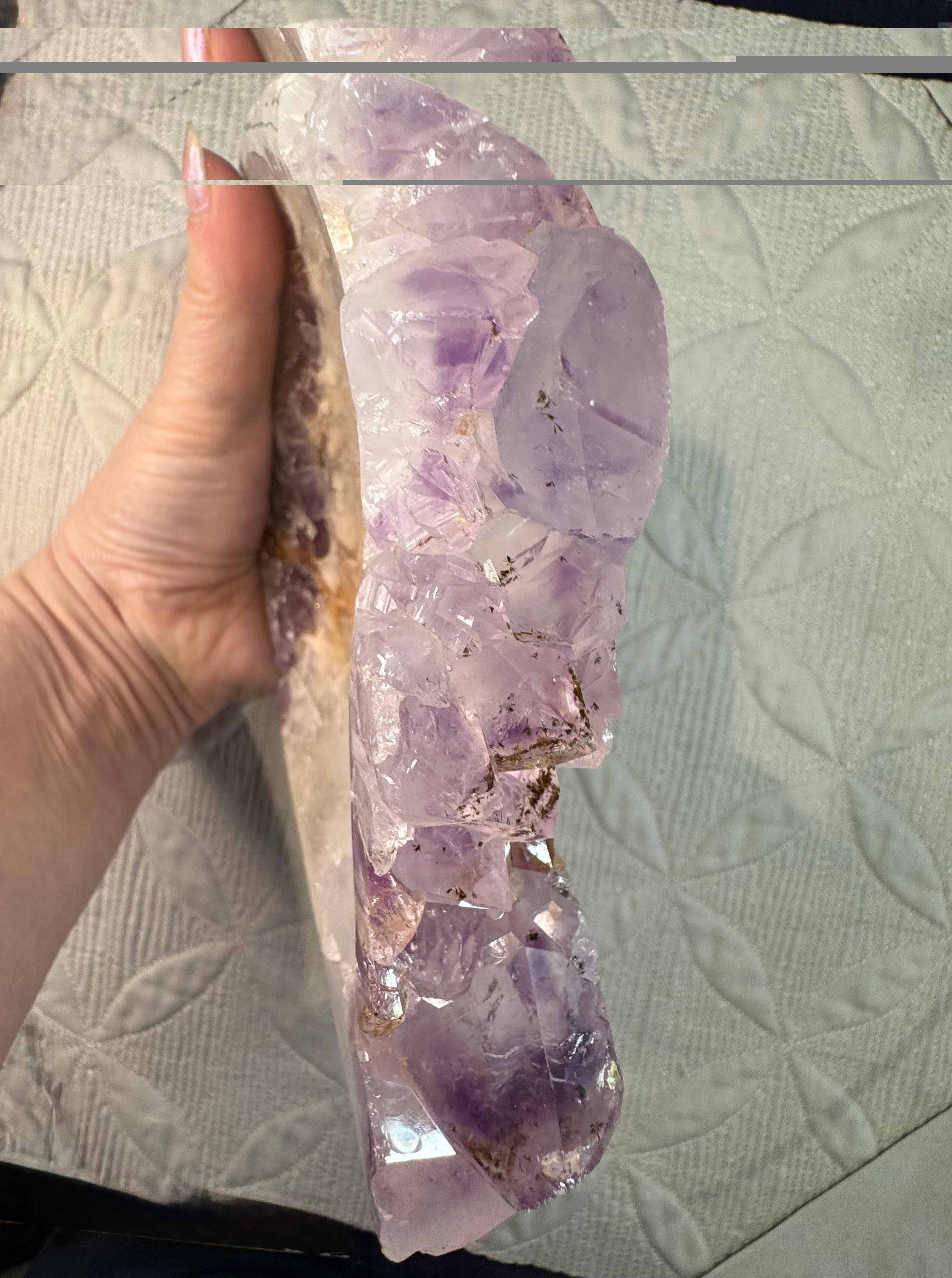 Amethyst crystal held by a hand on a textured surface